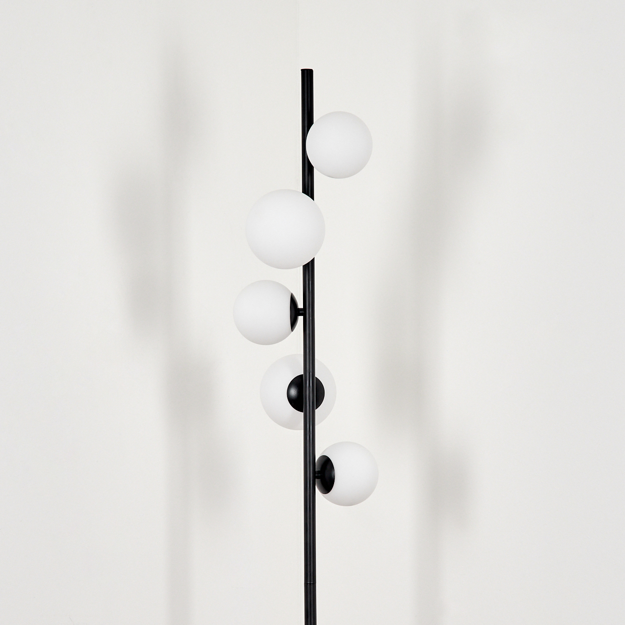 Eine moderne Stehlampe mit schwarzem Pfosten und fünf weißen Kugellampen. Schatten an der weißen Wand.