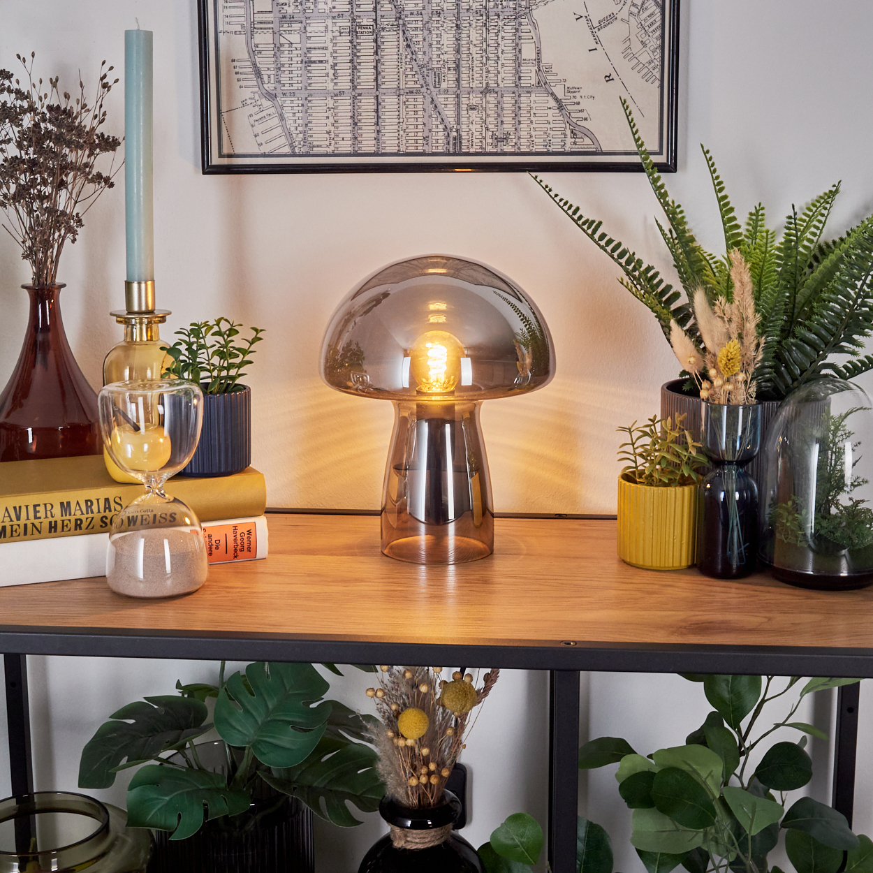 Eine pilzförmige Lampe steht auf einem Holzregal mit Pflanzen und Büchern. Im Hintergrund ist eine Karte zu sehen.