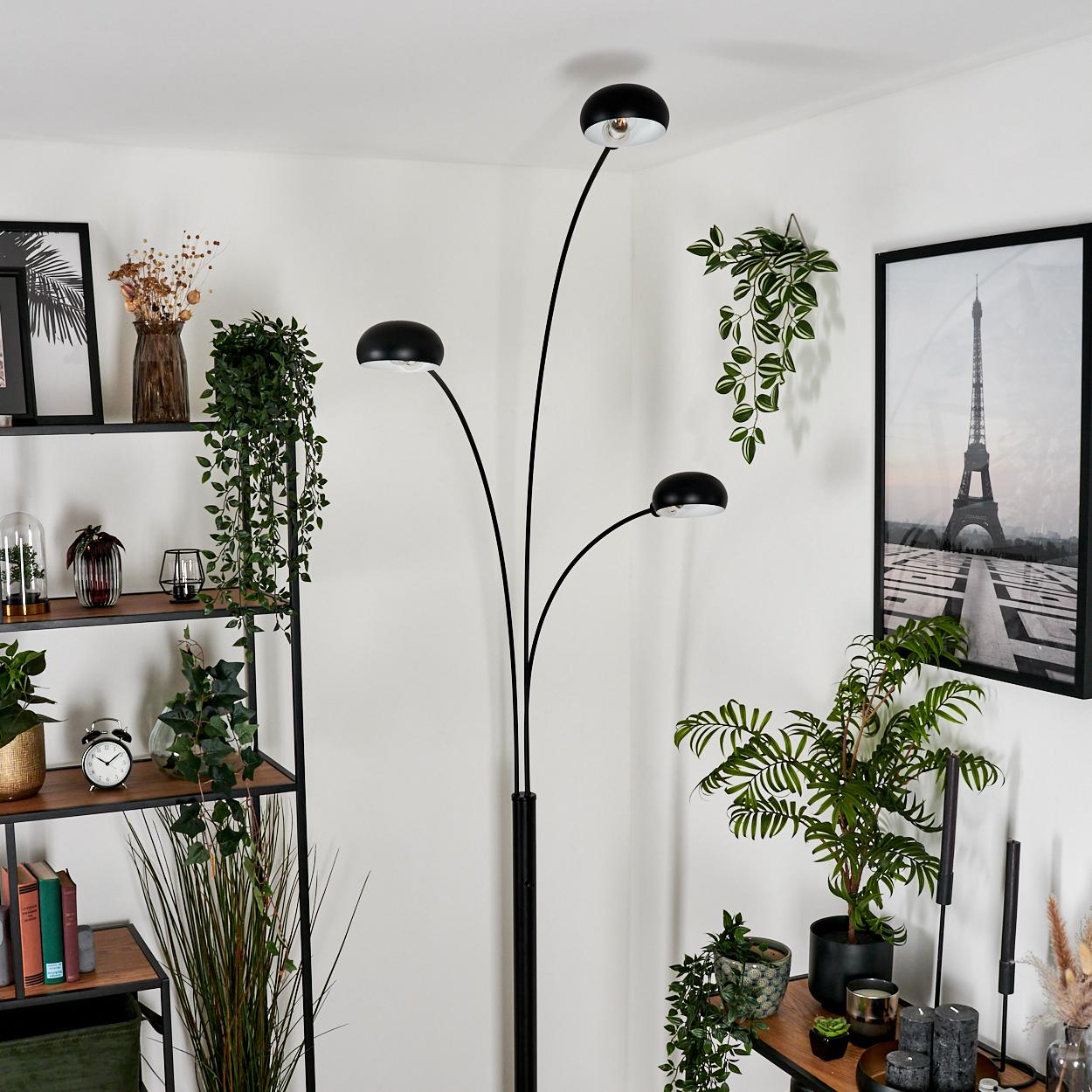 Eine schwarze Bogen-Stehlampe mit drei Lichtern befindet sich im Raum. Pflanzen und ein Bild des Eiffelturms sind ebenfalls zu sehen.
