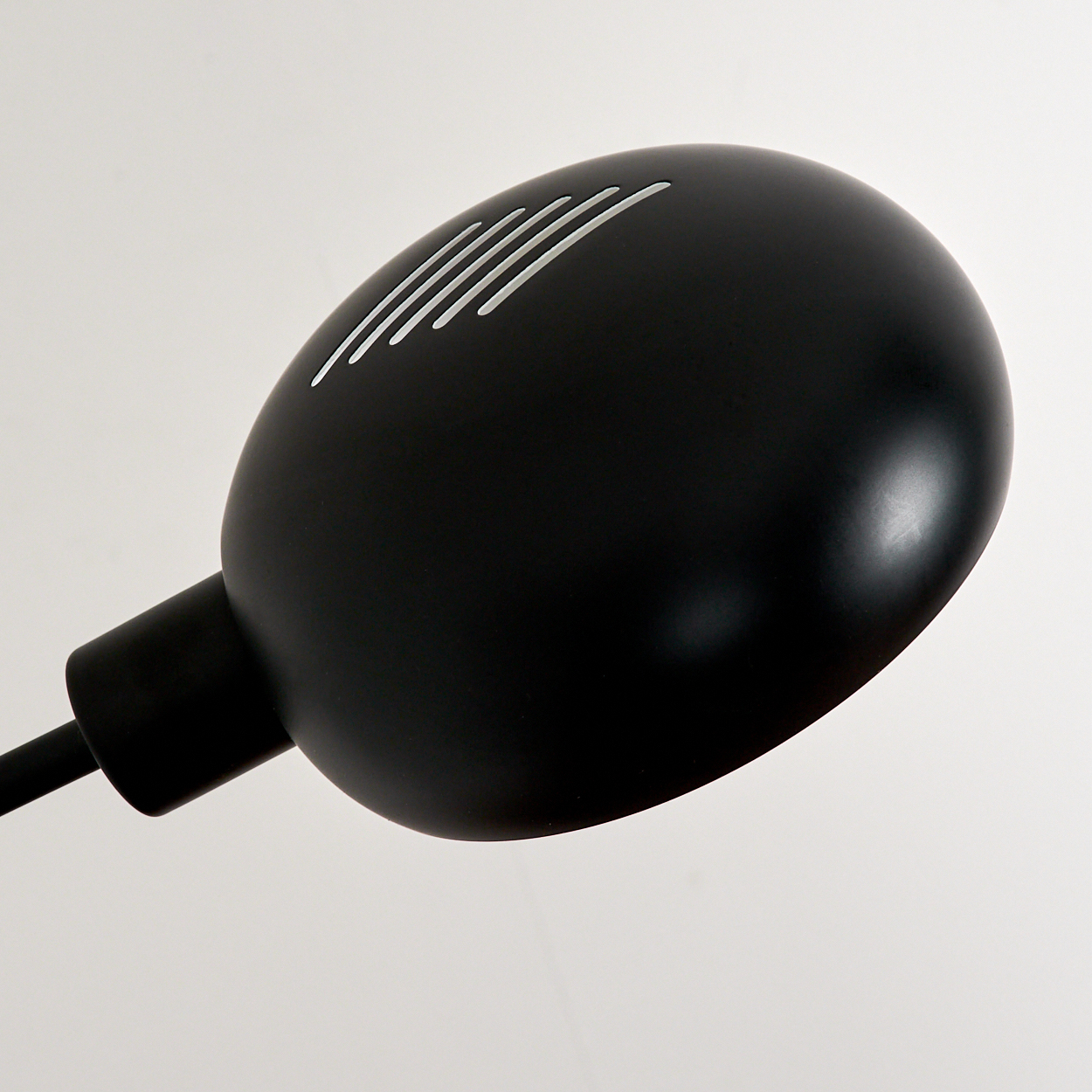 Nahaufnahme eines schwarzen Lampenkopfes mit weißen Streifen. Es ist vor einem weißen Hintergrund. Die Lampe ist nach oben geneigt.