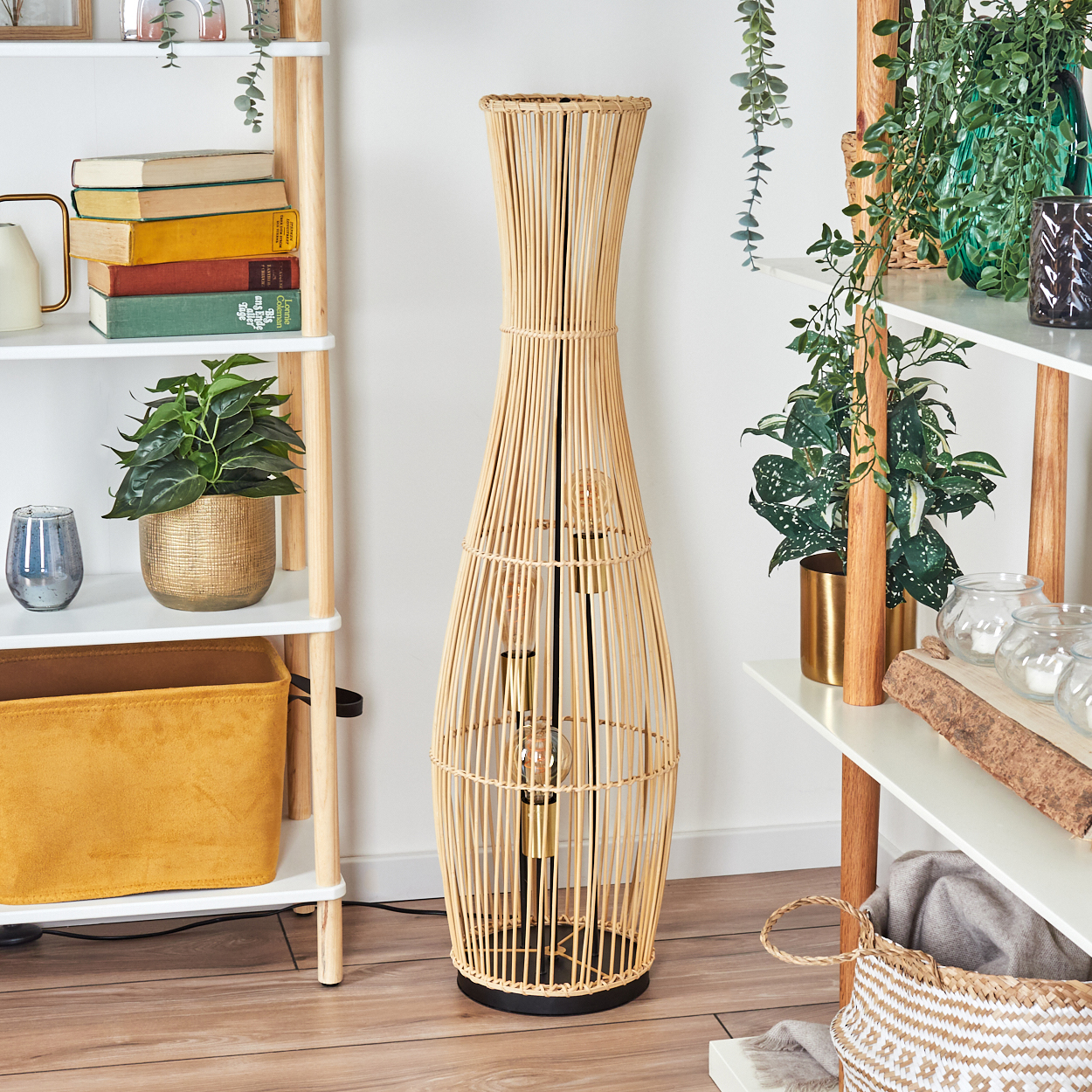 Eine hohe, gewebte Lampe steht im Mittelpunkt. Regale zeigen Bücher, Pflanzen und Dekorationsartikel. Der Raum hat ein warmes, einladendes Ambiente.