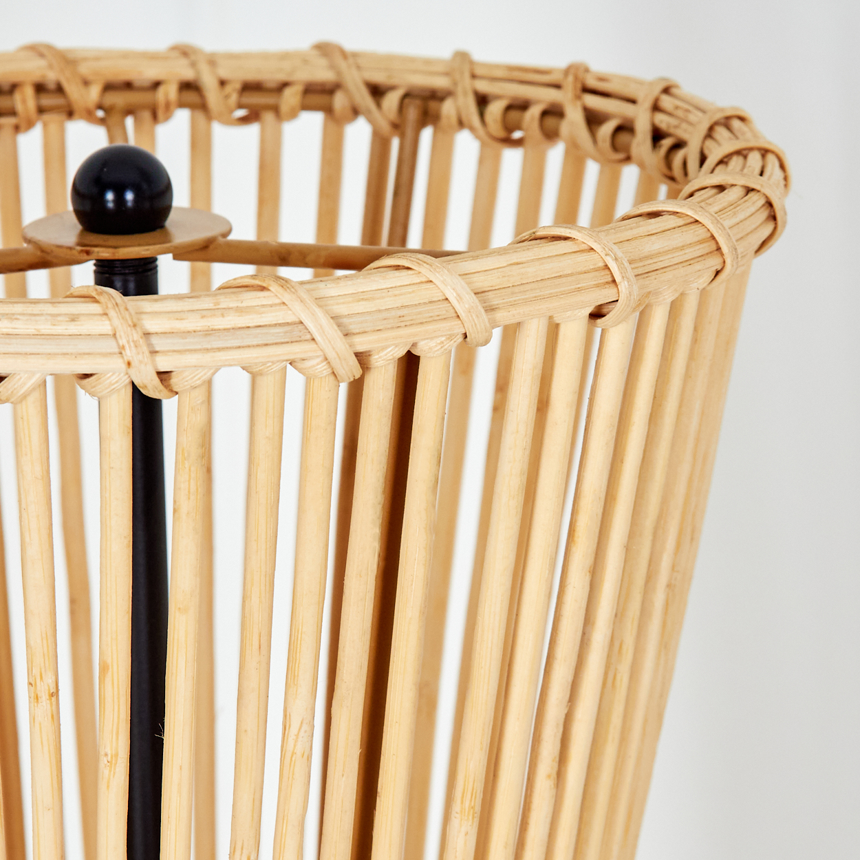Nahaufnahme eines gewebten Rattan-Lampenschirms. Eine schwarze vertikale Stange stützt den Schirm. Eine schwarze Kugel sitzt auf der Stange.