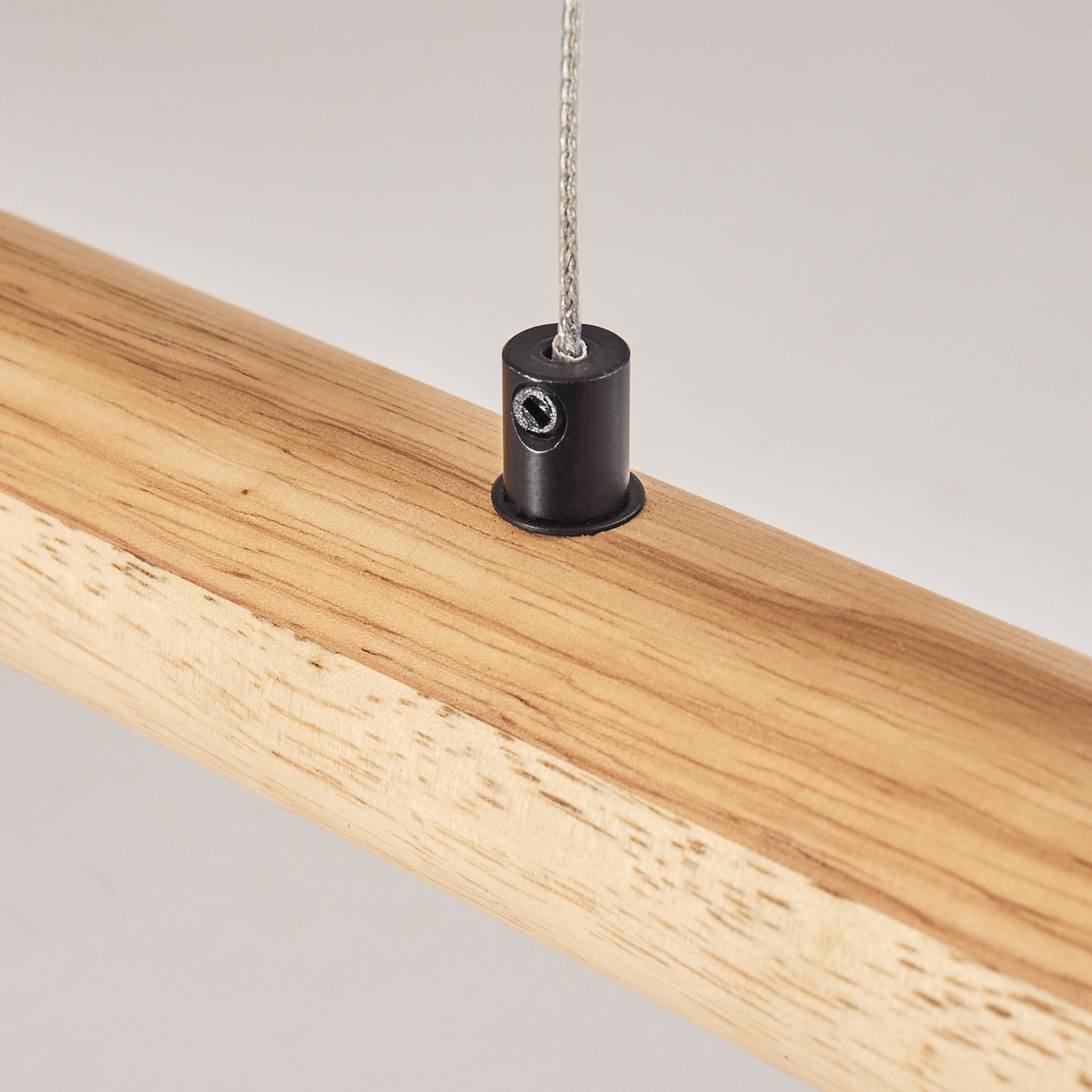Nahaufnahme eines Holzbalkens mit schwarzem Metallkabelhalter und einem silbernen Kabel, das herunterhängt. Weißer Hintergrund.