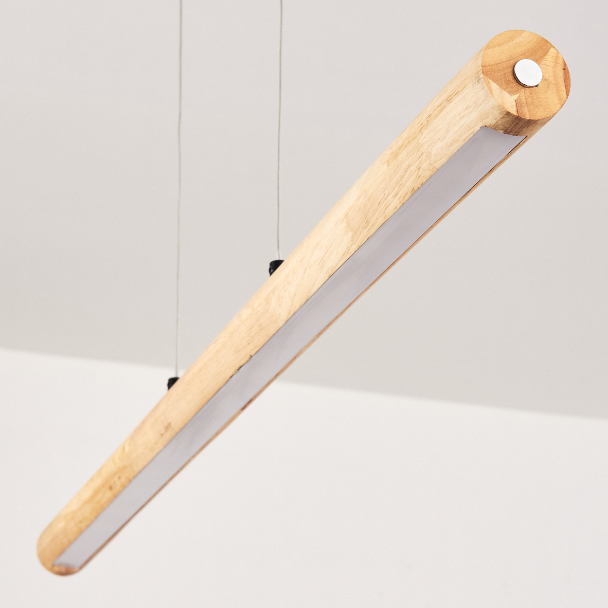 Eine zylindrische Holzleuchte hängt von der Decke. Sie hat einen weißen Lichtstreifen und ist an dünnen Drähten befestigt.