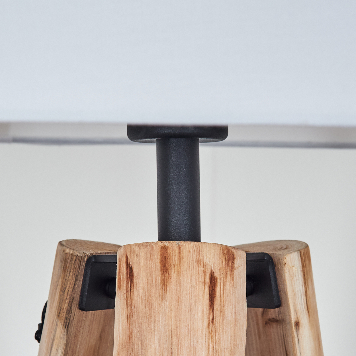 Ein Holzlampensockel mit einem schwarzen Mittelpfosten. Oben ist ein weißer Lampenschirm zu sehen. Der Sockel besteht aus Naturholz.