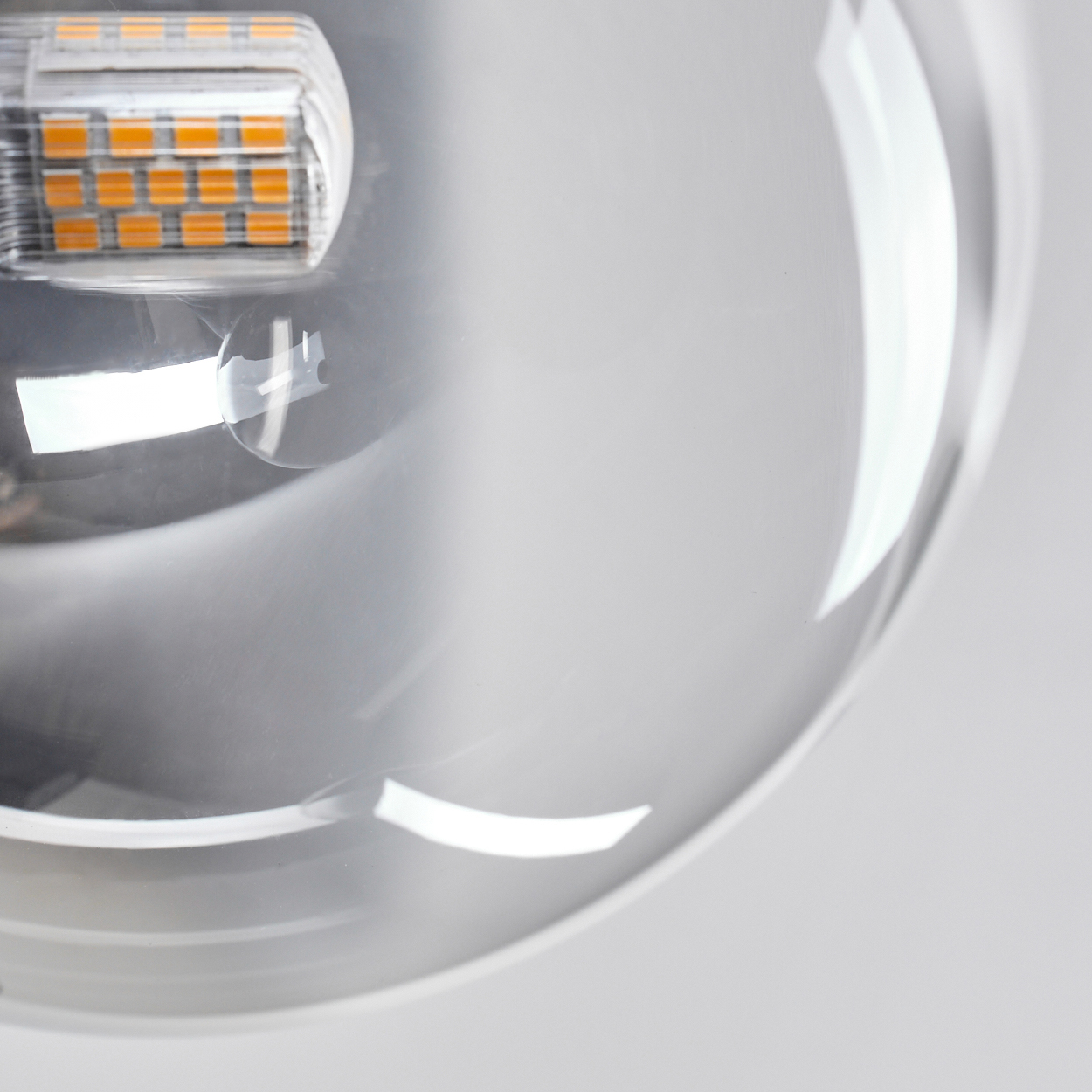Nahaufnahme eines Lampenschirms aus klarem Glas mit einer Lichtquelle. Die Lichtquelle hat orangefarbene LEDs. Der Hintergrund ist hellgrau.