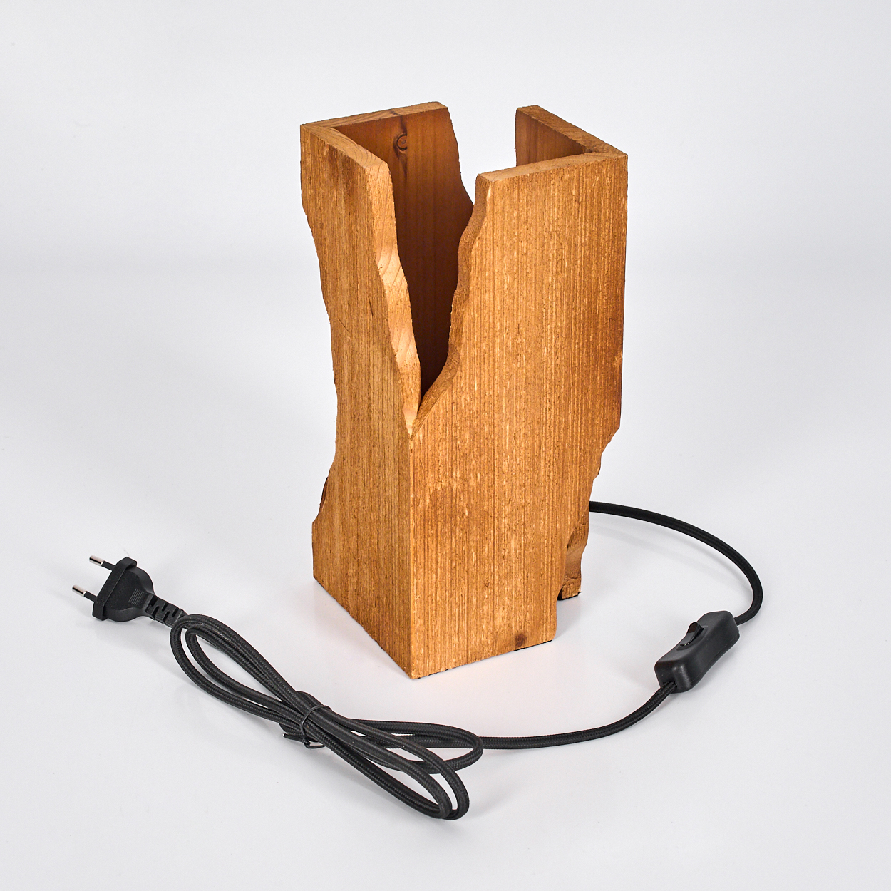 Eine Holzlampe mit rauer Kante, schwarzem Kabel und Schalter. Die Lampe steht auf einer weißen Oberfläche.