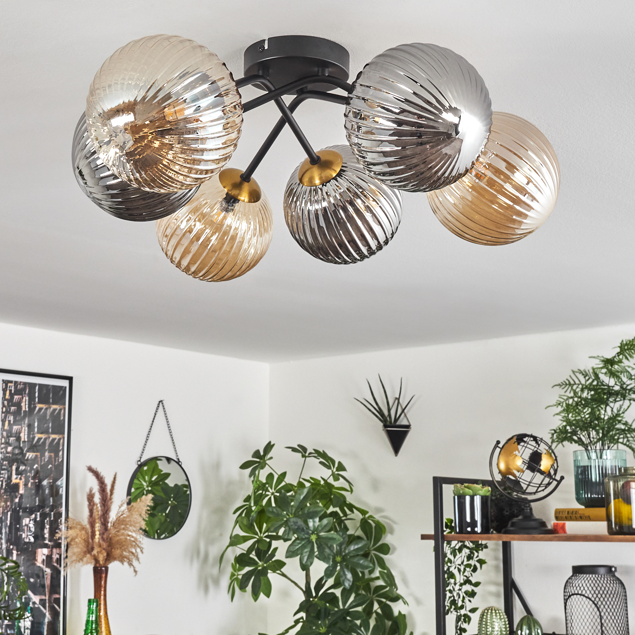Eine Deckenleuchte mit sechs Glasschirmkugeln. Der Raum hat Pflanzen, einen Spiegel, ein Regal mit Dekor und ein Bild an der Wand.