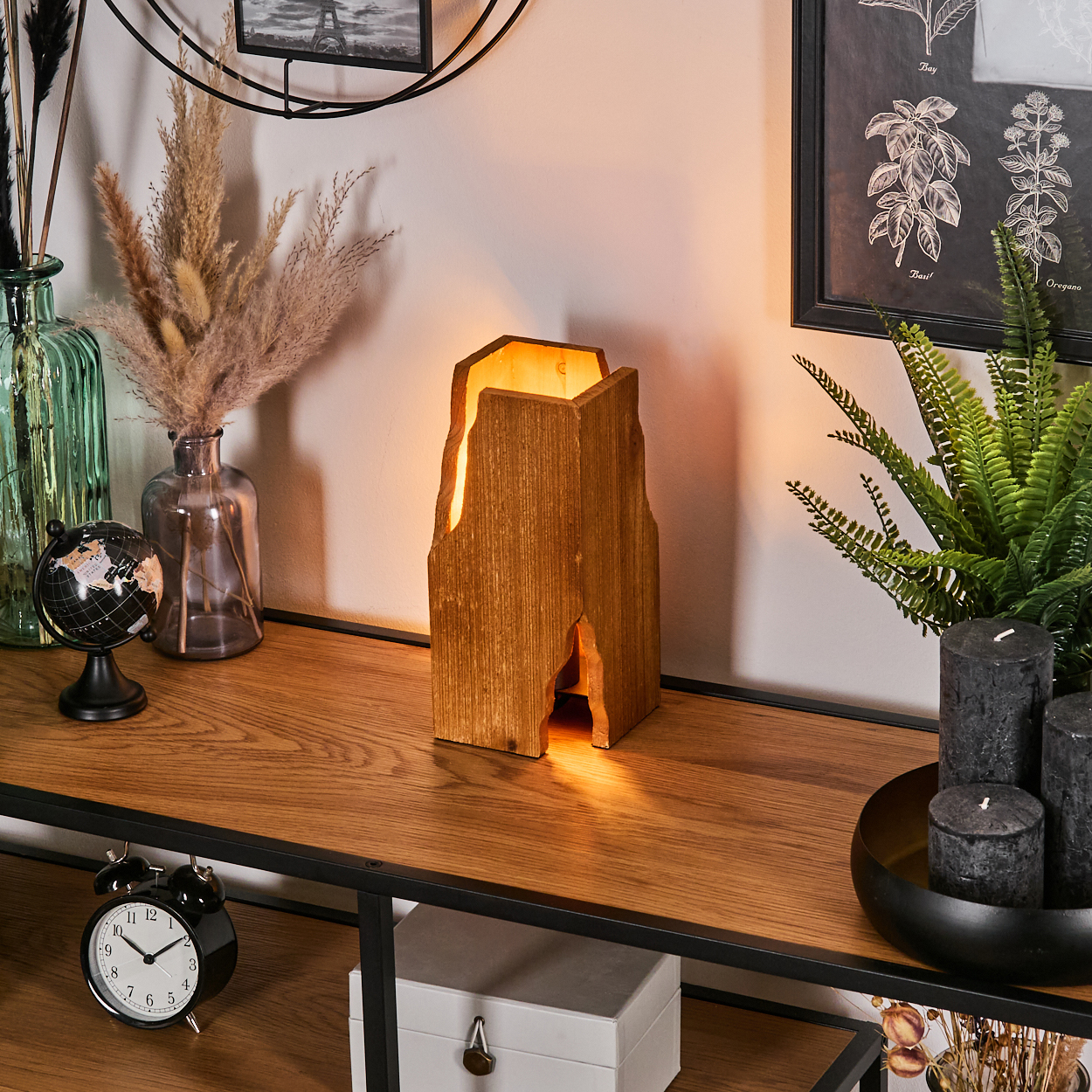 Holzlampe auf einem Holztisch. Weitere Gegenstände sind Kerzen, Pflanzen, Vasen, Globus und ein Wecker.