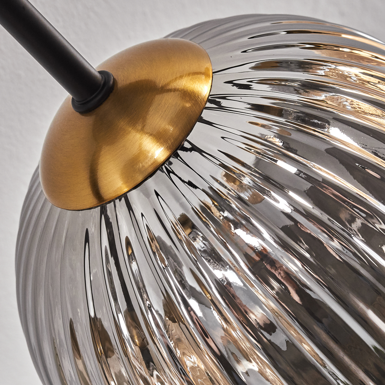 Nahaufnahme einer Lampe. Eine gerippte Glaskugel mit goldener Kappe ist an einem schwarzen Arm befestigt. Der Hintergrund ist weiß.
