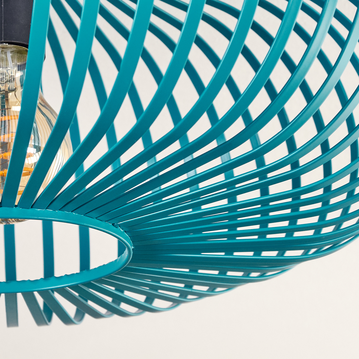 Nahaufnahme eines türkisfarbenen Metalllampenschirms mit Spiraldesign. Eine Edison-Glühbirne ist sichtbar. Weißer Hintergrund.