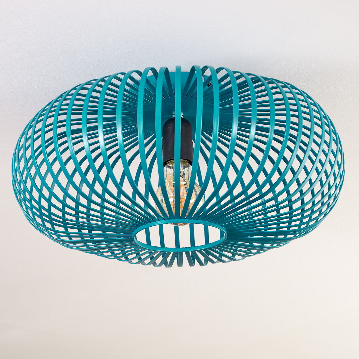 Eine türkisfarbene, käfigartige Deckenlampe mit sichtbarer Glühbirne. Sie ist an einer weißen Decke befestigt. Die Lampe hat ein kreisförmiges Design.