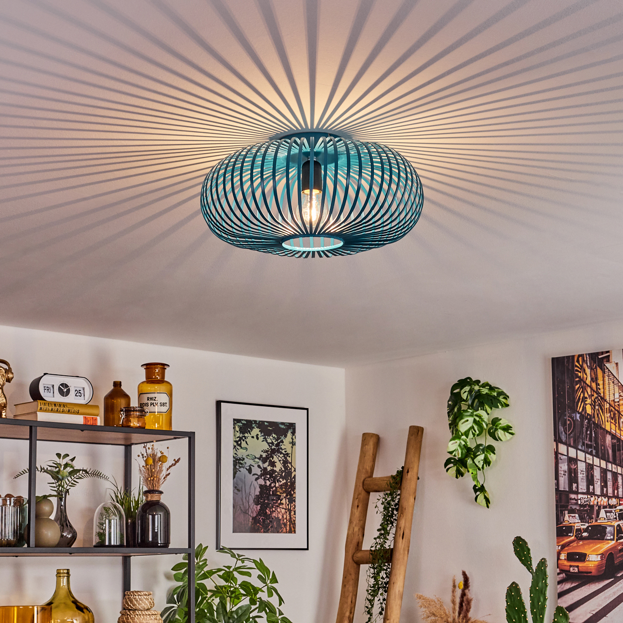 Eine türkisfarbene Deckenlampe wirft Schatten. Regale mit Deko, eine Leiter, Pflanzen und ein Bilderrahmen sind sichtbar. Der Raum ist hell.