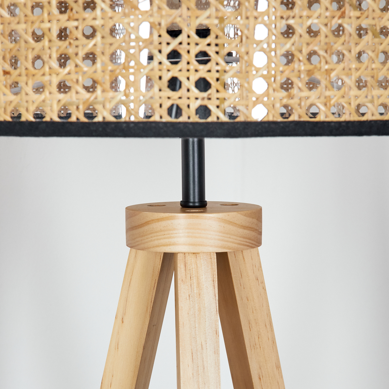 Nahaufnahme einer Lampe mit gewebtem Lampenschirm und Holzstativfuß. Der Lampenschirm ist beige und schwarz, der Fuß aus Naturholz.