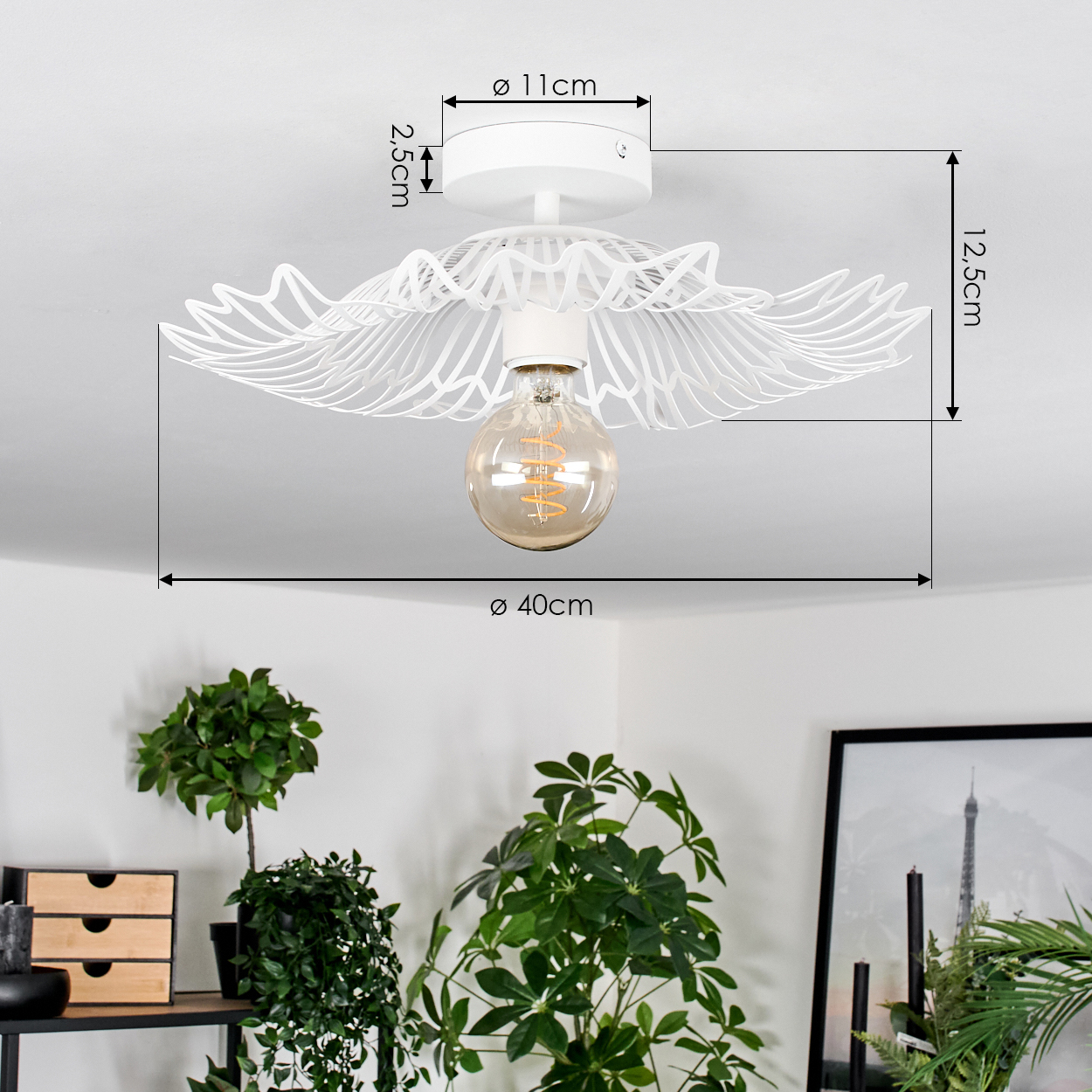 Weiße Deckenlampe mit dekorativem Design und freiliegender Glühbirne. Pflanzen und Möbel befinden sich im Vordergrund, vor einer weißen Wand.