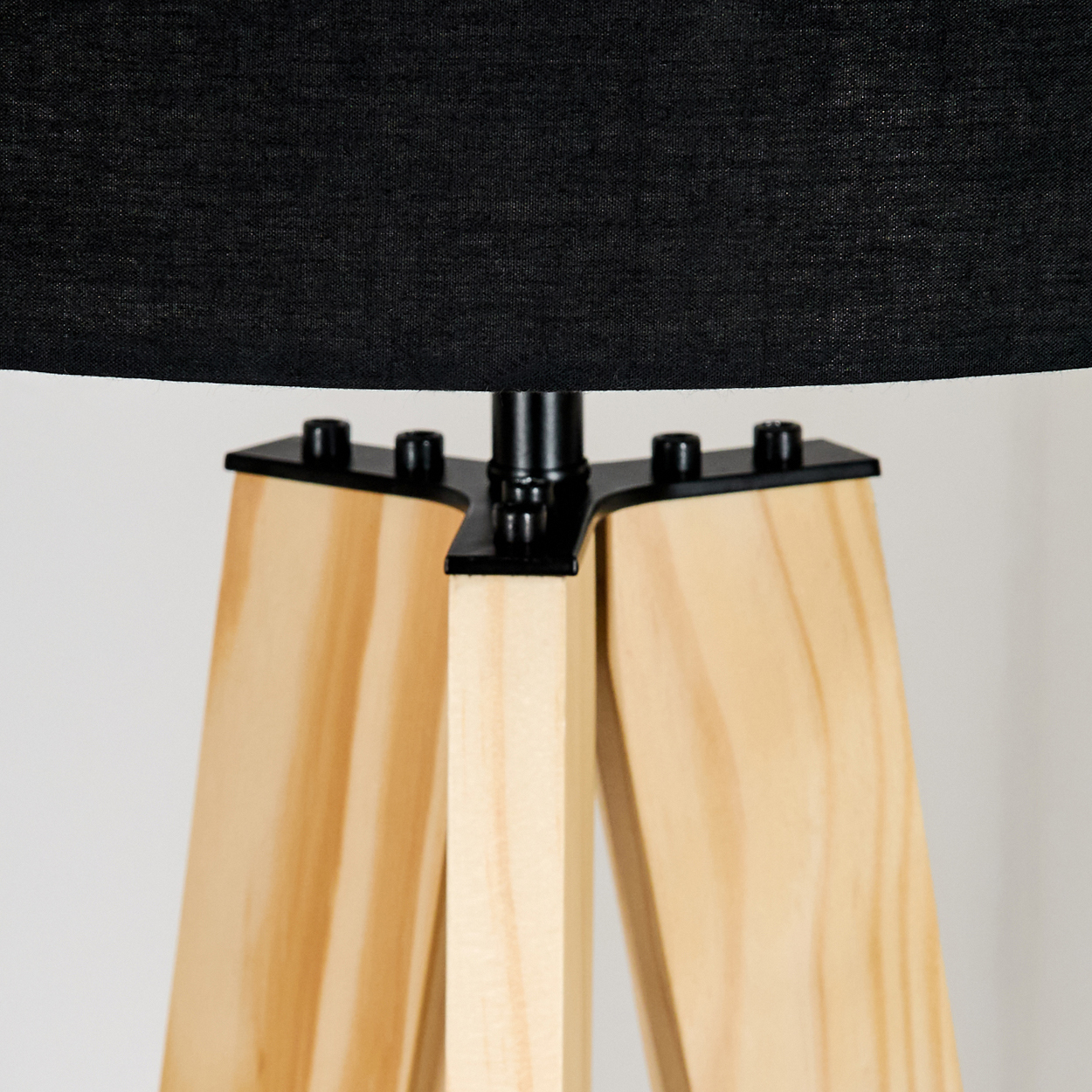 Nahaufnahme einer Lampe mit schwarzem Lampenschirm und Holzbeinen. Die Lampe steht vor weißem Hintergrund.
