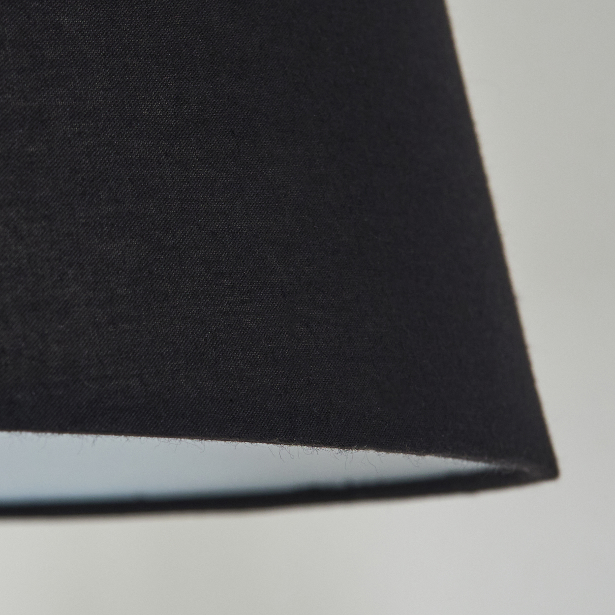 Nahaufnahme eines schwarzen Lampenschirms mit hellblauem Innenraum vor weißem Hintergrund. Der Lampenschirm ist abgewinkelt.