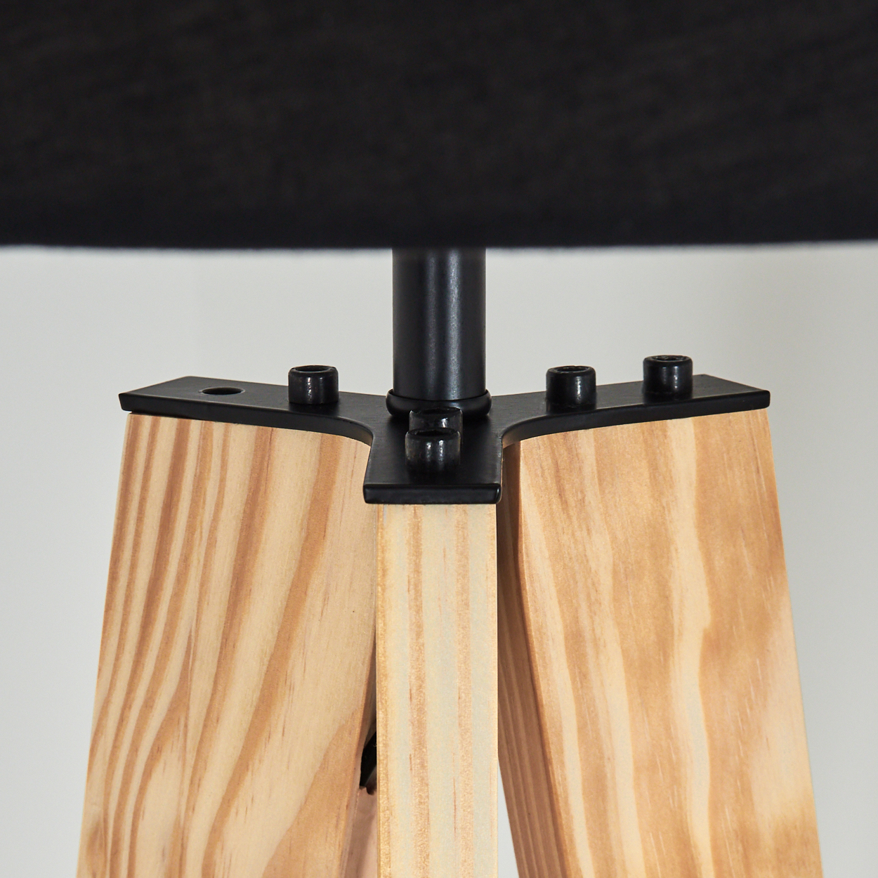 Ein Lampensockel aus Holz mit schwarzen Metallakzenten und einem schwarzen Lampenschirm. Der Sockel hat drei Holzbeine und schwarze Metallschrauben.