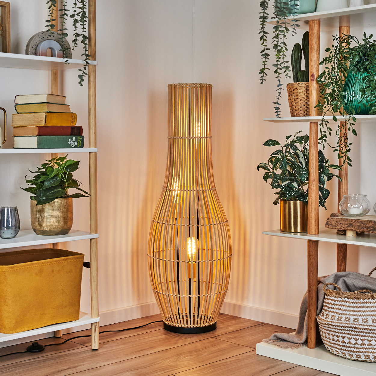 Eine hohe, gewebte Bambuslampe ist der Mittelpunkt. Regale mit Pflanzen und Büchern flankieren sie. Holzfußboden, gelbe Aufbewahrung und Hängepflanzen.