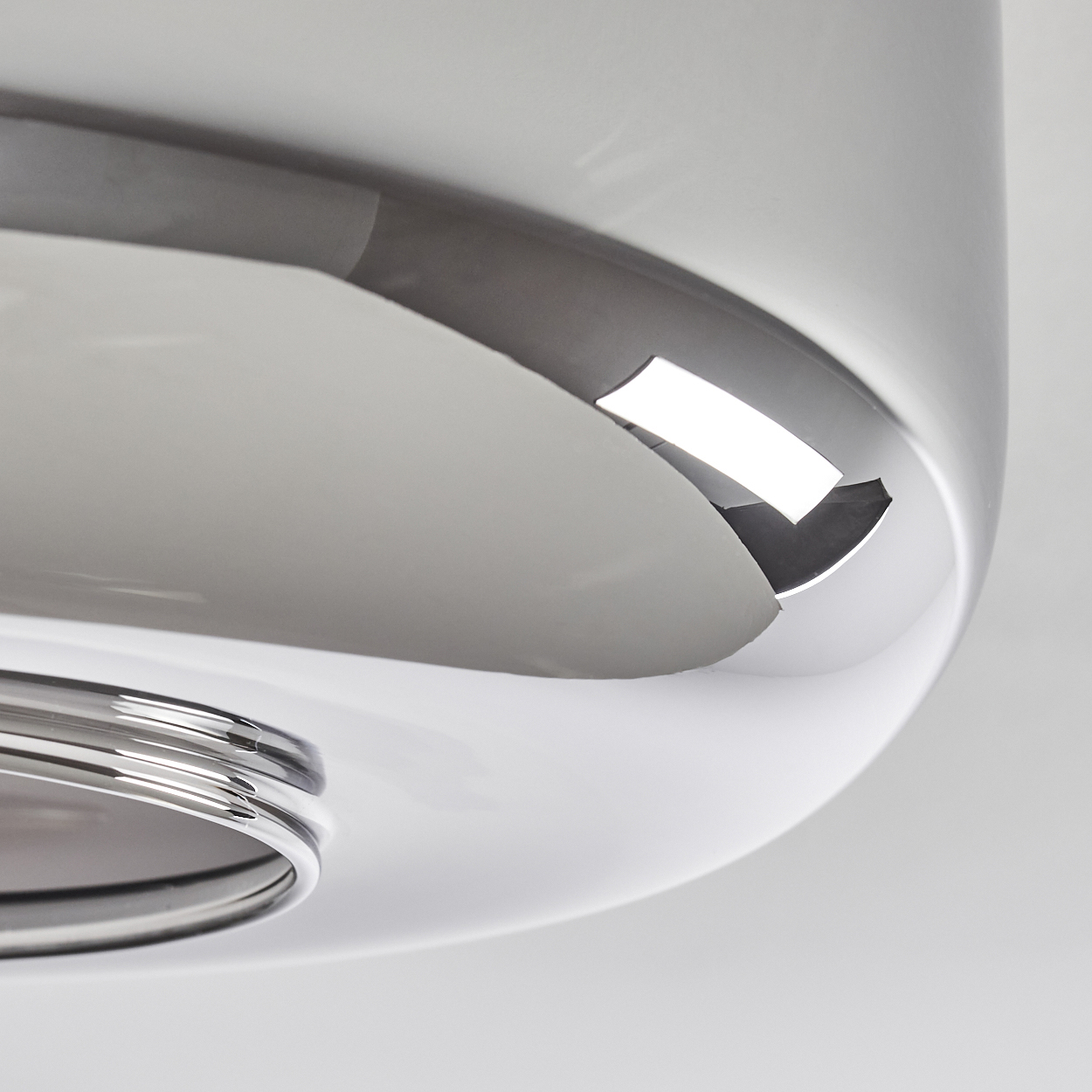 Nahaufnahme eines polierten, chromartigen Objekts mit weißen und grauen Oberflächen, die Licht reflektieren. Das Objekt hat ein kreisförmiges Design mit Kurven.