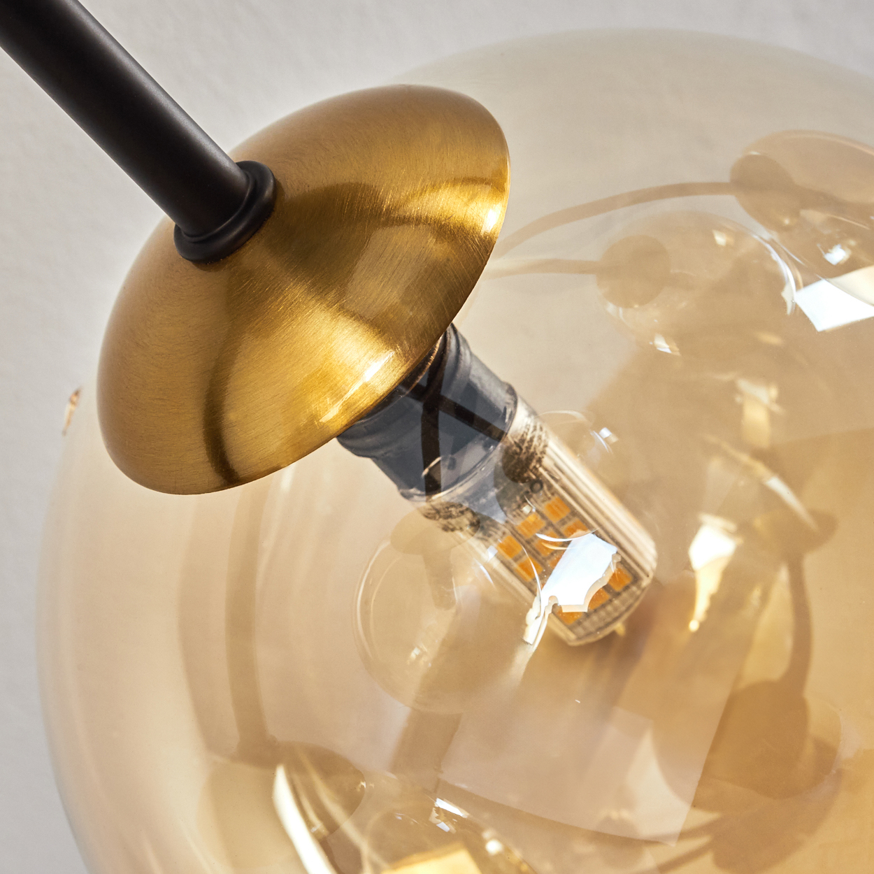 Nahaufnahme einer modernen Leuchte mit goldenem Schirm und klarem, kugelförmigem Glas. Im Inneren ist eine kleine LED-Glühbirne zu sehen.