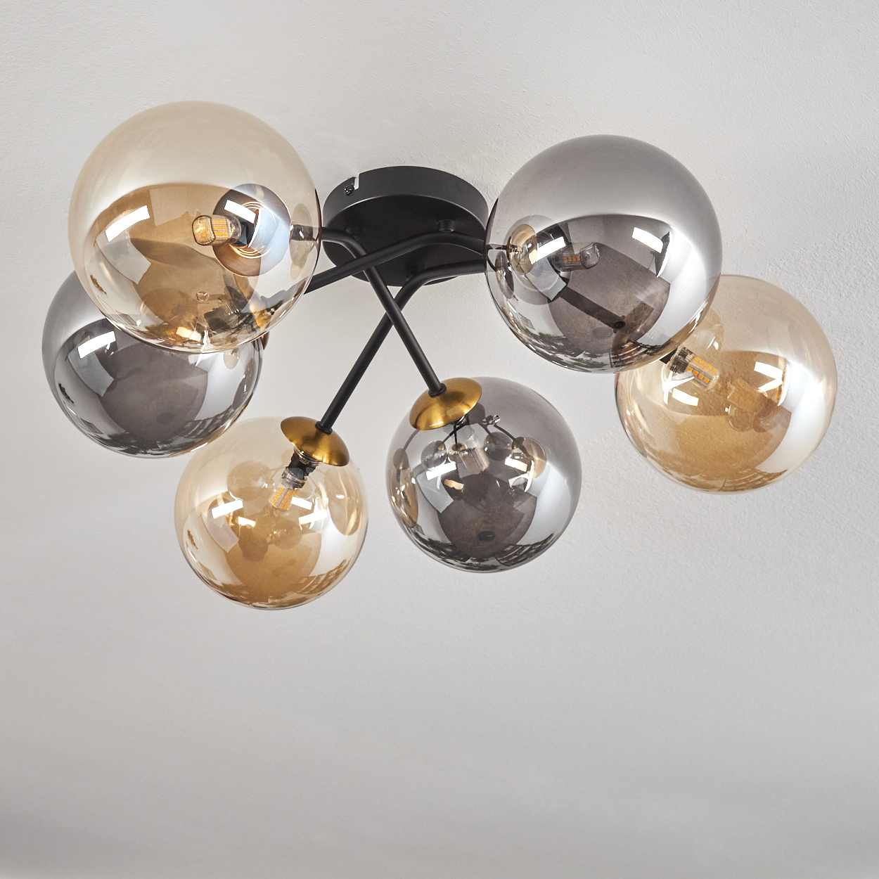Eine moderne Deckenleuchte mit sechs kugelförmigen Schirmen in Gold und Silber, angeordnet auf schwarzen Armen, vor weißem Hintergrund.