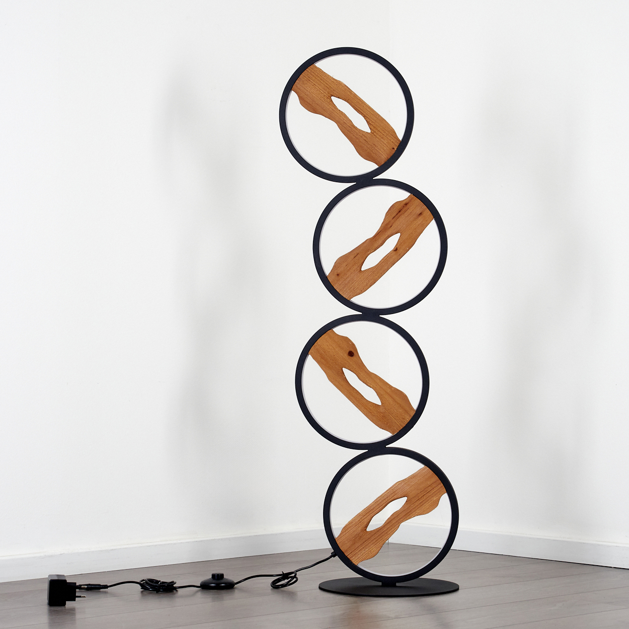 Eine moderne Lampe mit vier gestapelten kreisförmigen Rahmen. Jeder Rahmen hat ein Holzdesign im Inneren. Die Lampe steht auf Holzboden.
