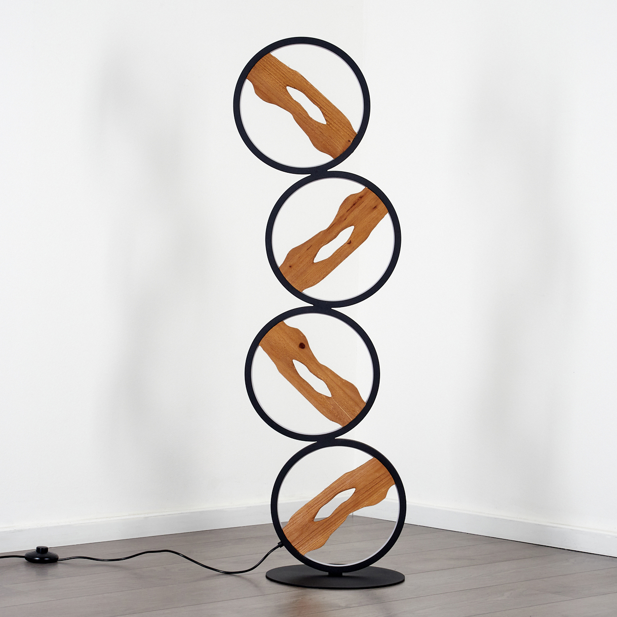 Eine moderne Stehlampe mit vier kreisförmigen Rahmen. Jeder Rahmen hat ein Holzdesign. Die Lampe steht auf einem Holzboden.