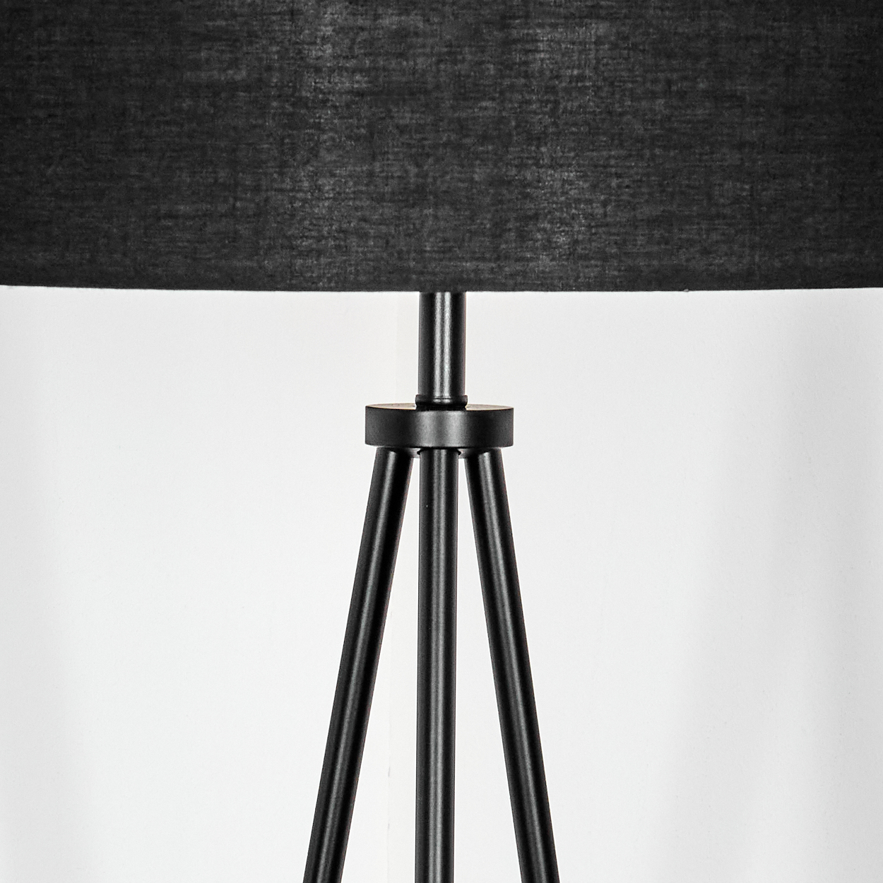 Ein schwarzer Lampenschirm mit schwarzem Stativfuß. Der Hintergrund ist eine schlichte weiße Wand. Die Lampe ist zentriert.
