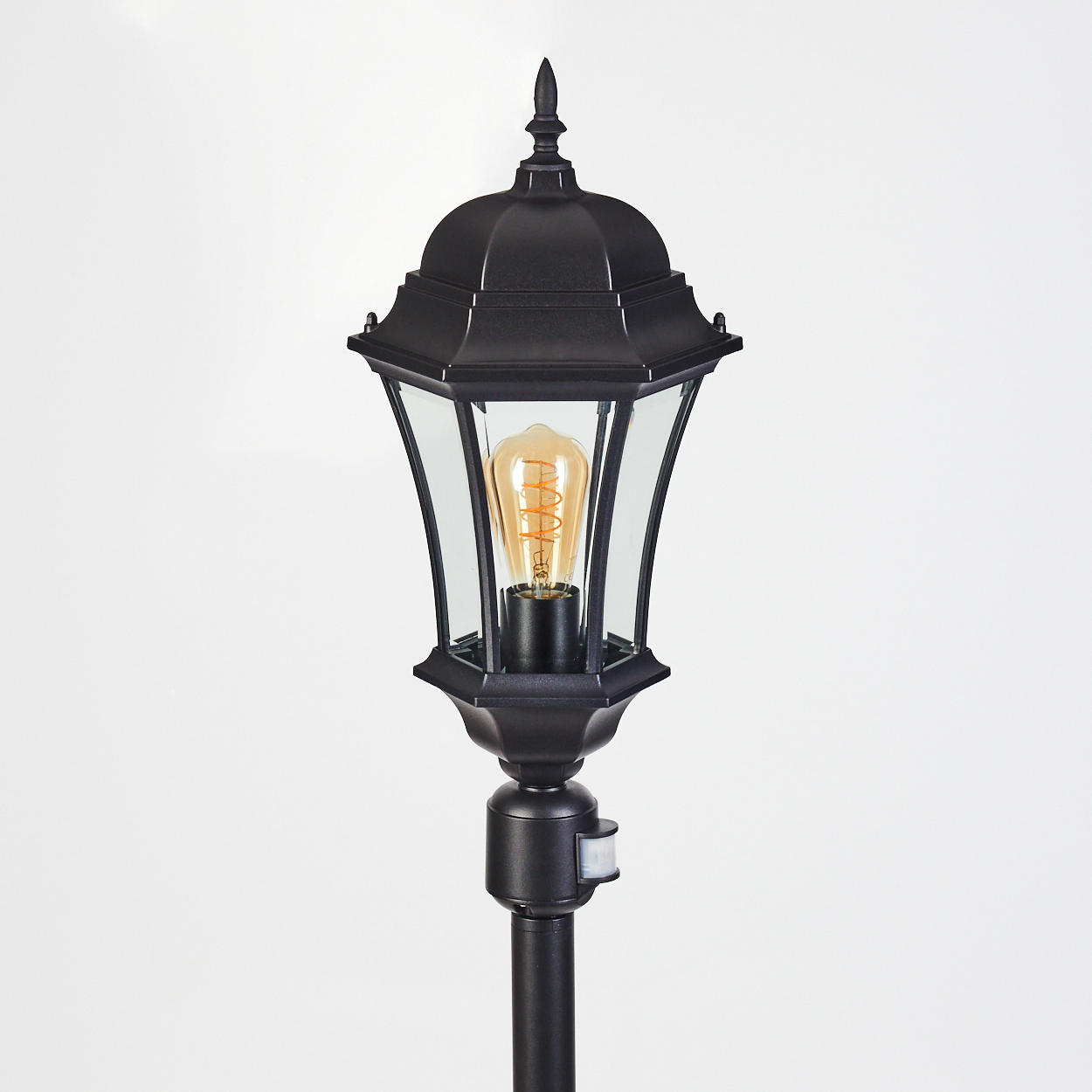 Eine schwarze Außenlaterne mit einer leuchtenden Glühbirne, vor einem weißen Hintergrund. Die Lampe hat ein klassisches Design.