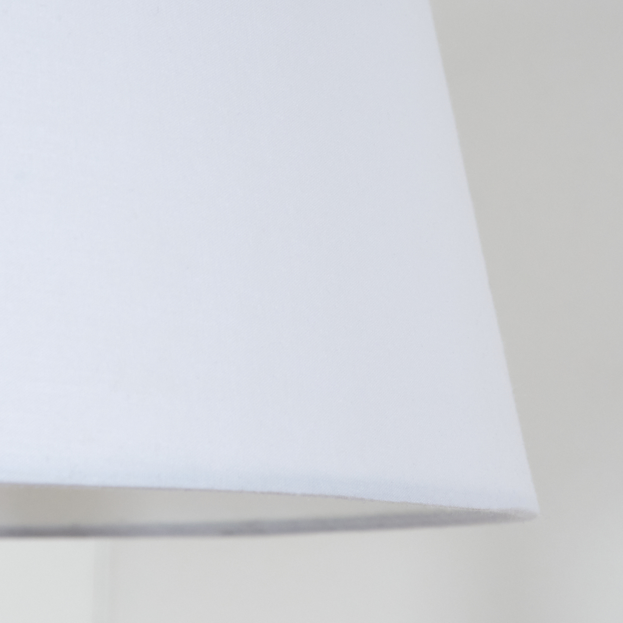 Nahaufnahme eines weißen Lampenschirms mit leicht strukturierter Oberfläche. Der Hintergrund ist eine schlichte, hellfarbige Wand.