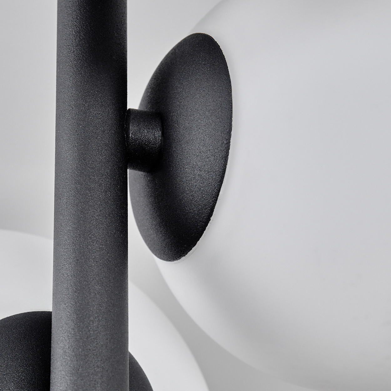 Nahaufnahme einer modernen Lampe. Schwarzer Metallrahmen trägt weiße, kugelförmige Schirme. Eine schwarze Scheibe verbindet.