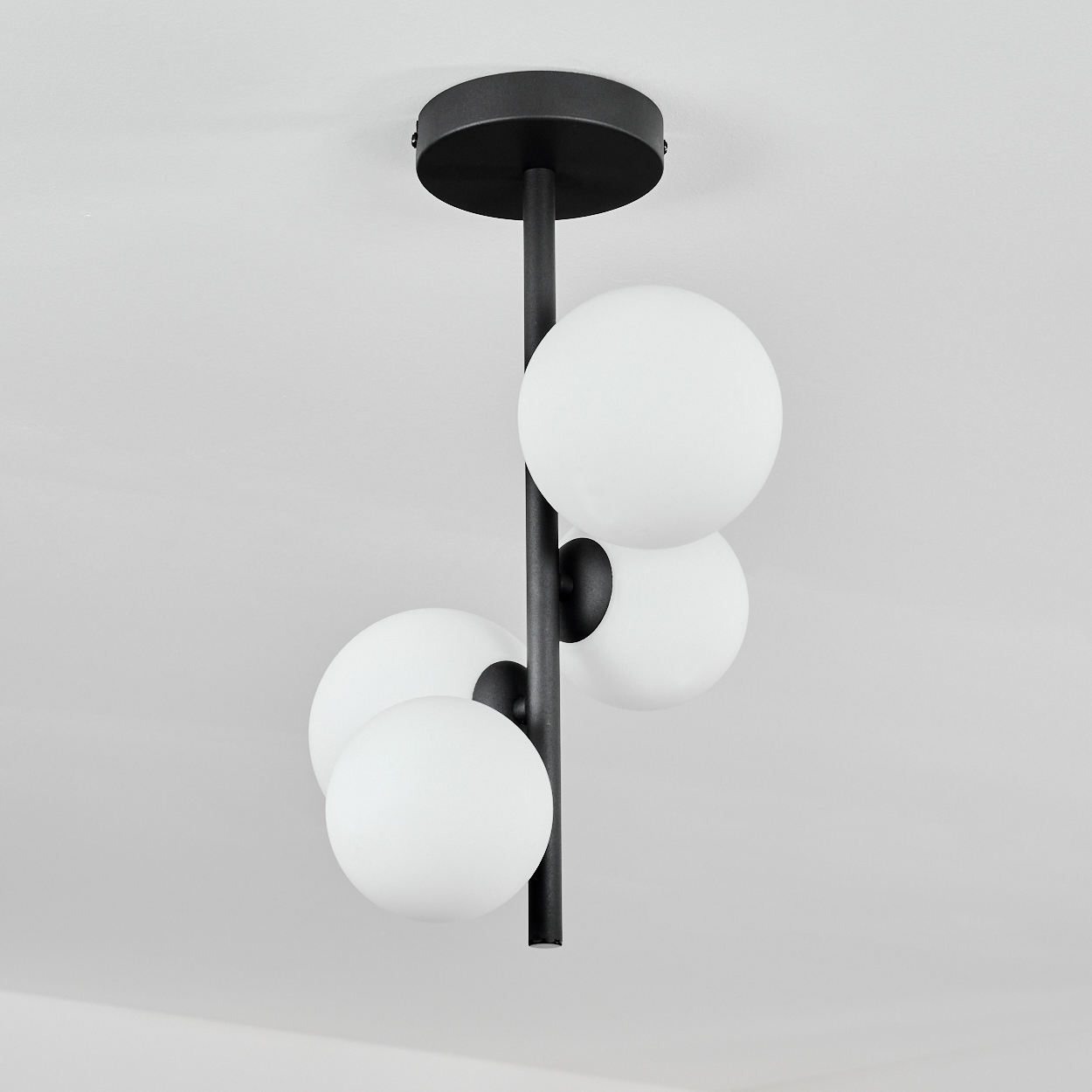 Deckenleuchte. Schwarze Metallstange mit vier weißen, kugelförmigen Lampen. An einer weißen Decke montiert.