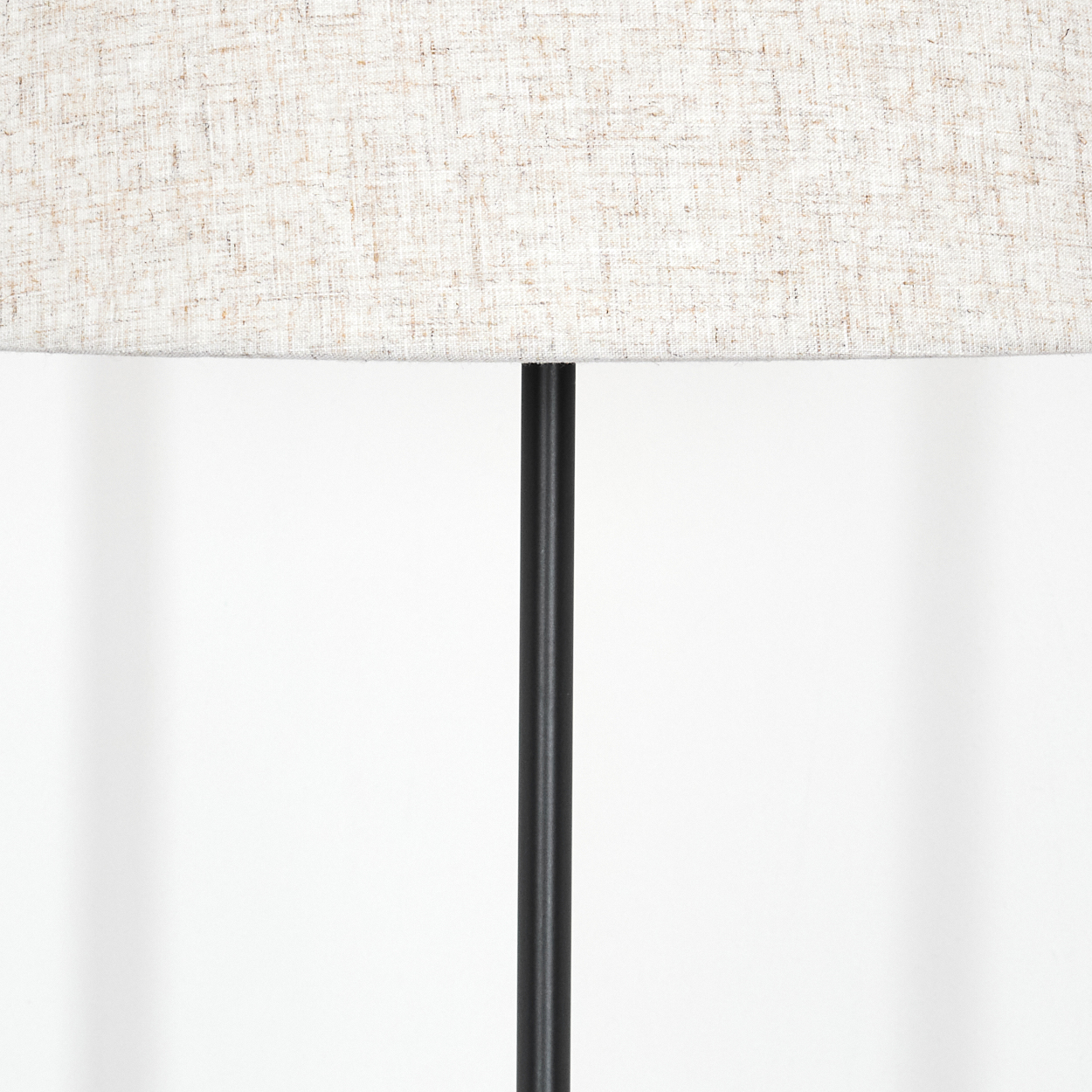 Nahaufnahme einer Lampe. Ein beigefarbener Lampenschirm sitzt über einer schwarzen Stange. Der Hintergrund ist weiß.