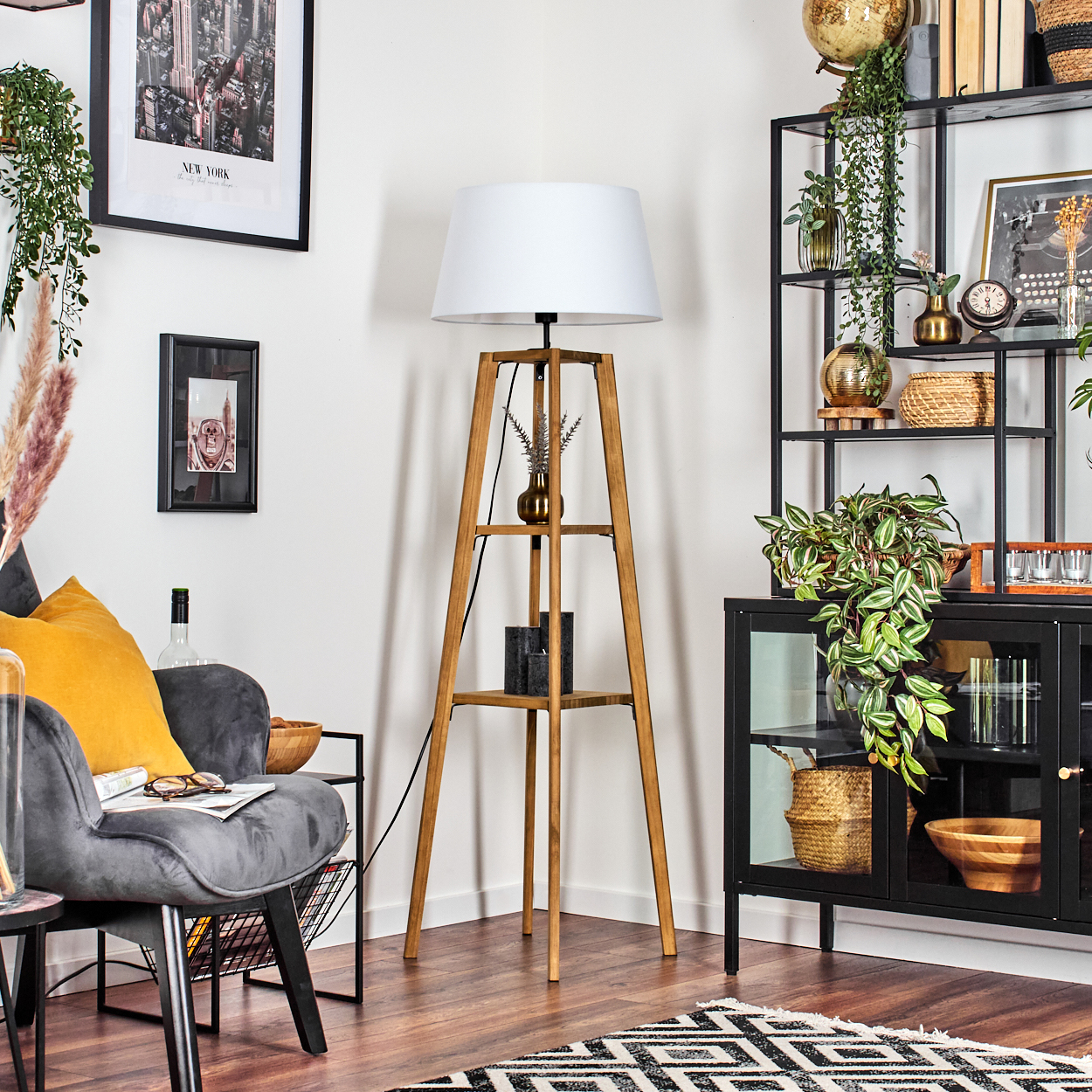 Wohnzimmer mit Holzlampe, grauem Stuhl und schwarzem Bücherregal. Ein Teppich, Kunst und Pflanzen vervollständigen die gemütliche Szene.