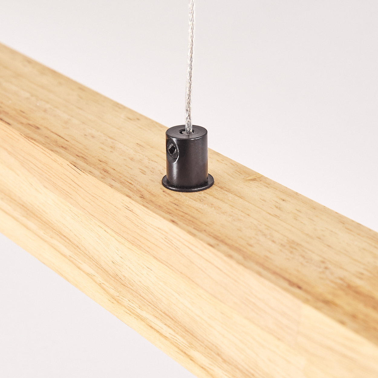 Nahaufnahme eines Holzbalkens mit schwarzem Metallbeschlag und Draht. Der Balken ist hellbraun, der Hintergrund weiß.