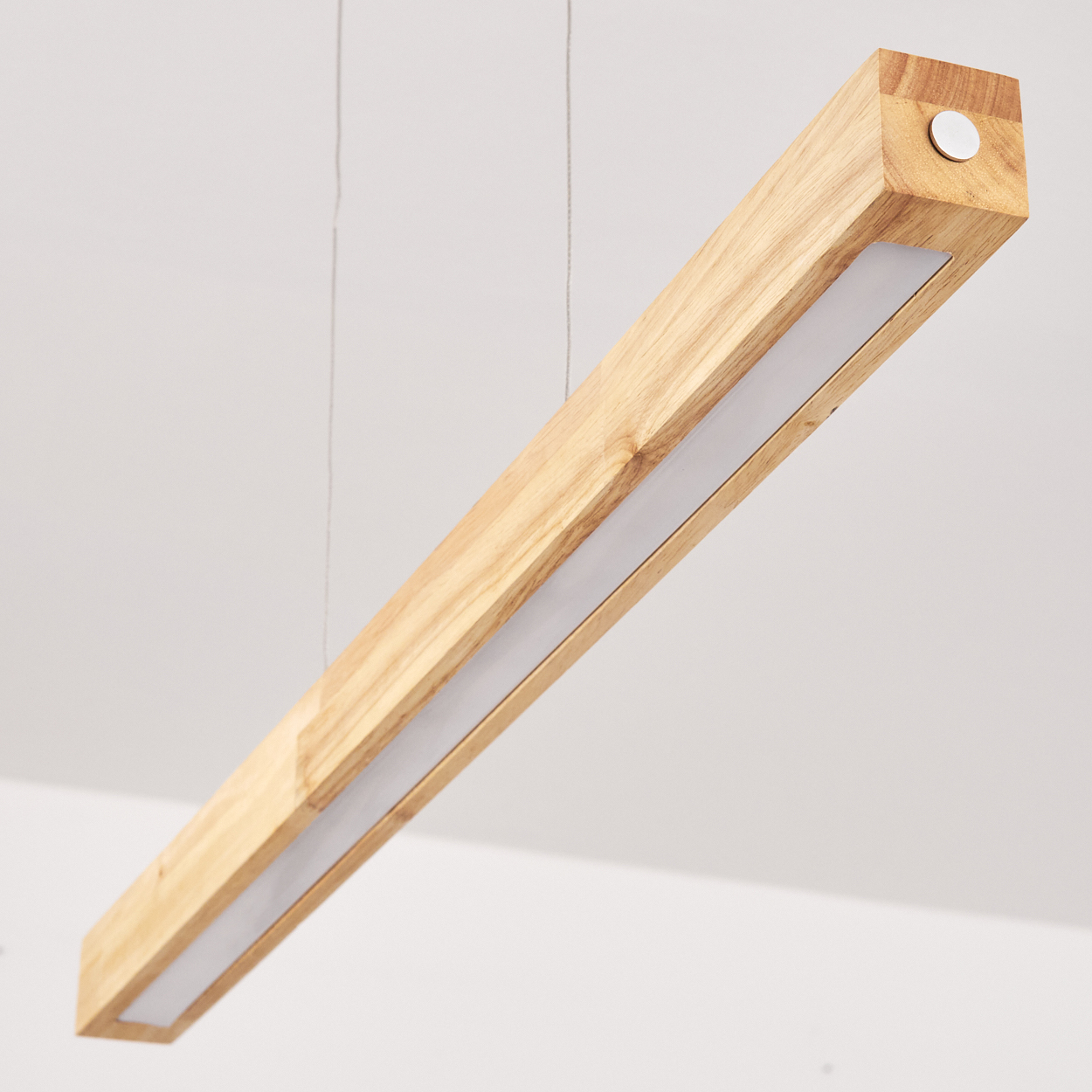 Eine hölzerne, rechteckige Leuchte hängt von der Decke. Sie hat einen hellen weißen Lichtstreifen und einen kleinen Metallknopf am Ende.