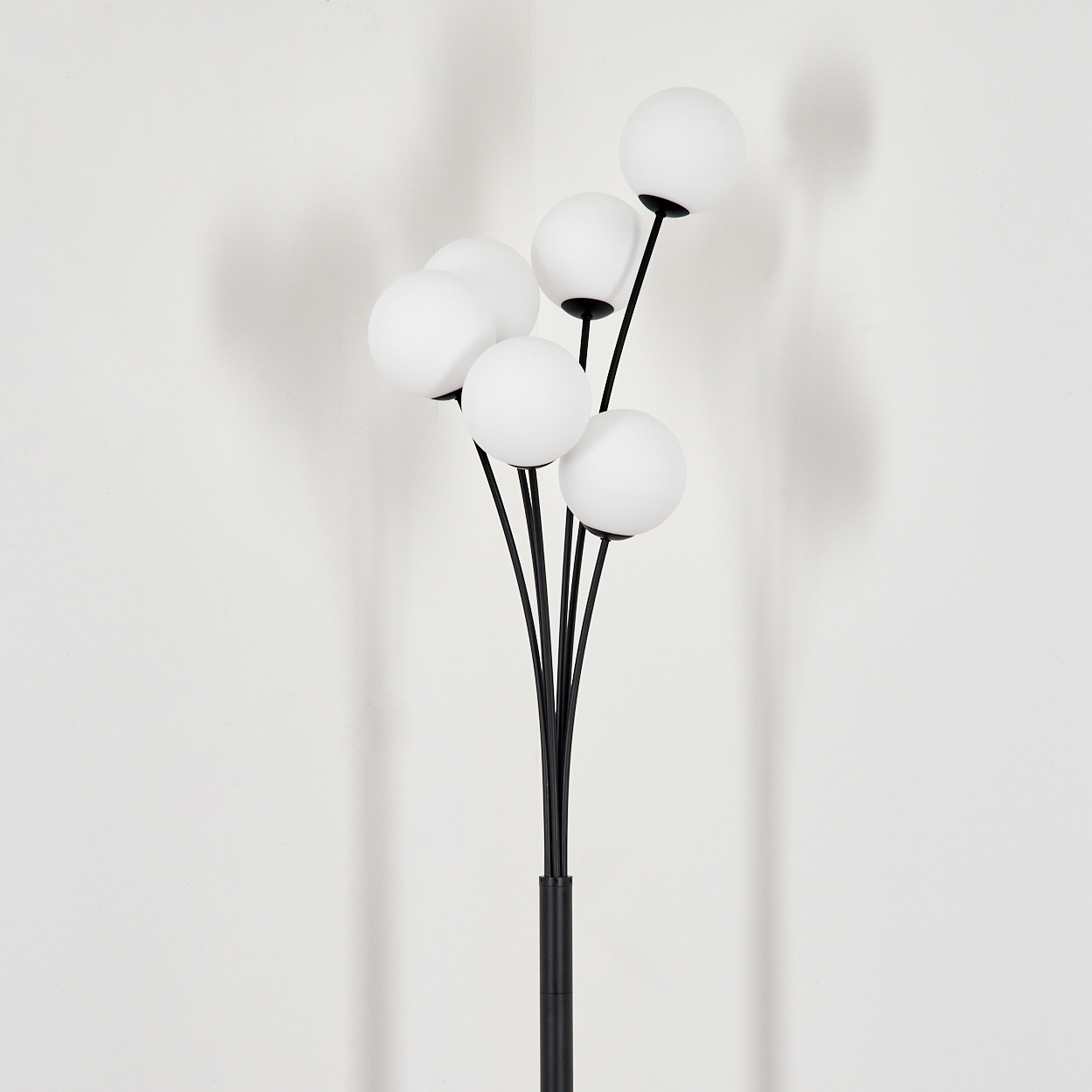 Eine schwarze Lampe mit mehreren weißen Kugellampen. Die Lampe steht vor einer weißen Wand mit einem Schatten der Lampe.