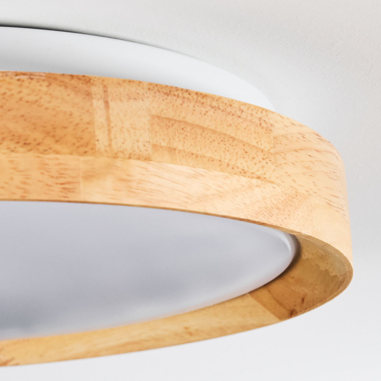 Nahaufnahme einer Deckenleuchte. Sie hat einen Holzring um den weißen Lichtdiffusor. Der Hintergrund ist eine weiße Decke.