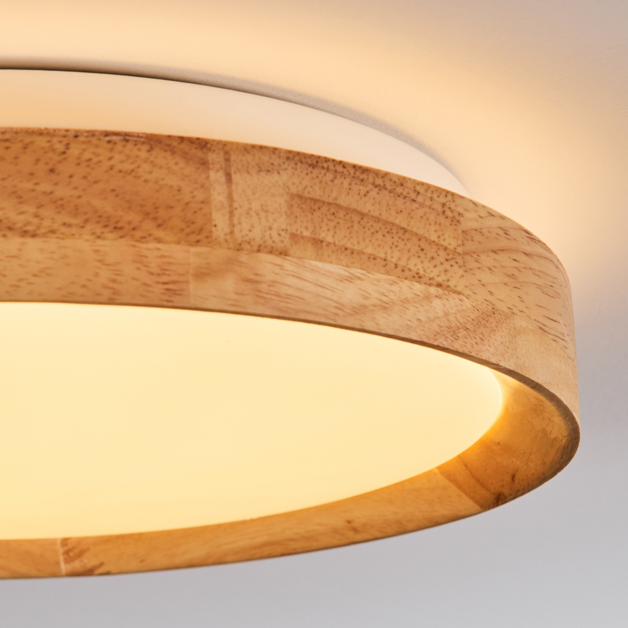 Nahaufnahme einer modernen Deckenleuchte. Sie hat einen Holzrahmen, einen weißen Rand und eine weiche, leuchtende Lichtfläche.