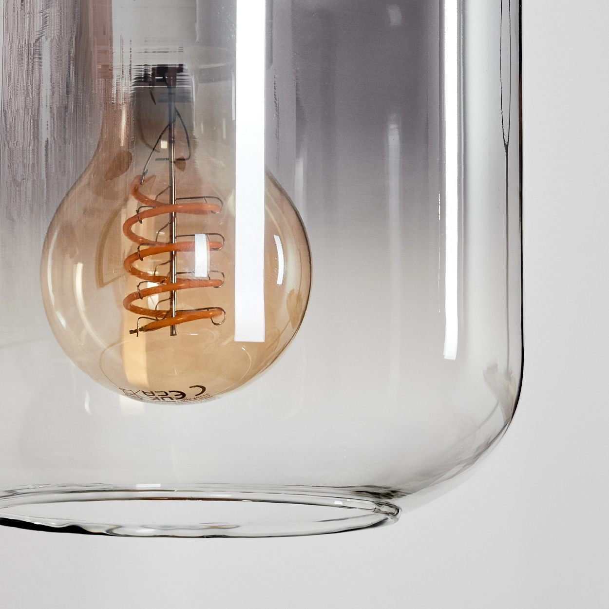 Eine Glühbirne in einem transparenten Lampenschirm. Die Glühbirne hat einen dekorativen, orangefarbenen Glühfaden.