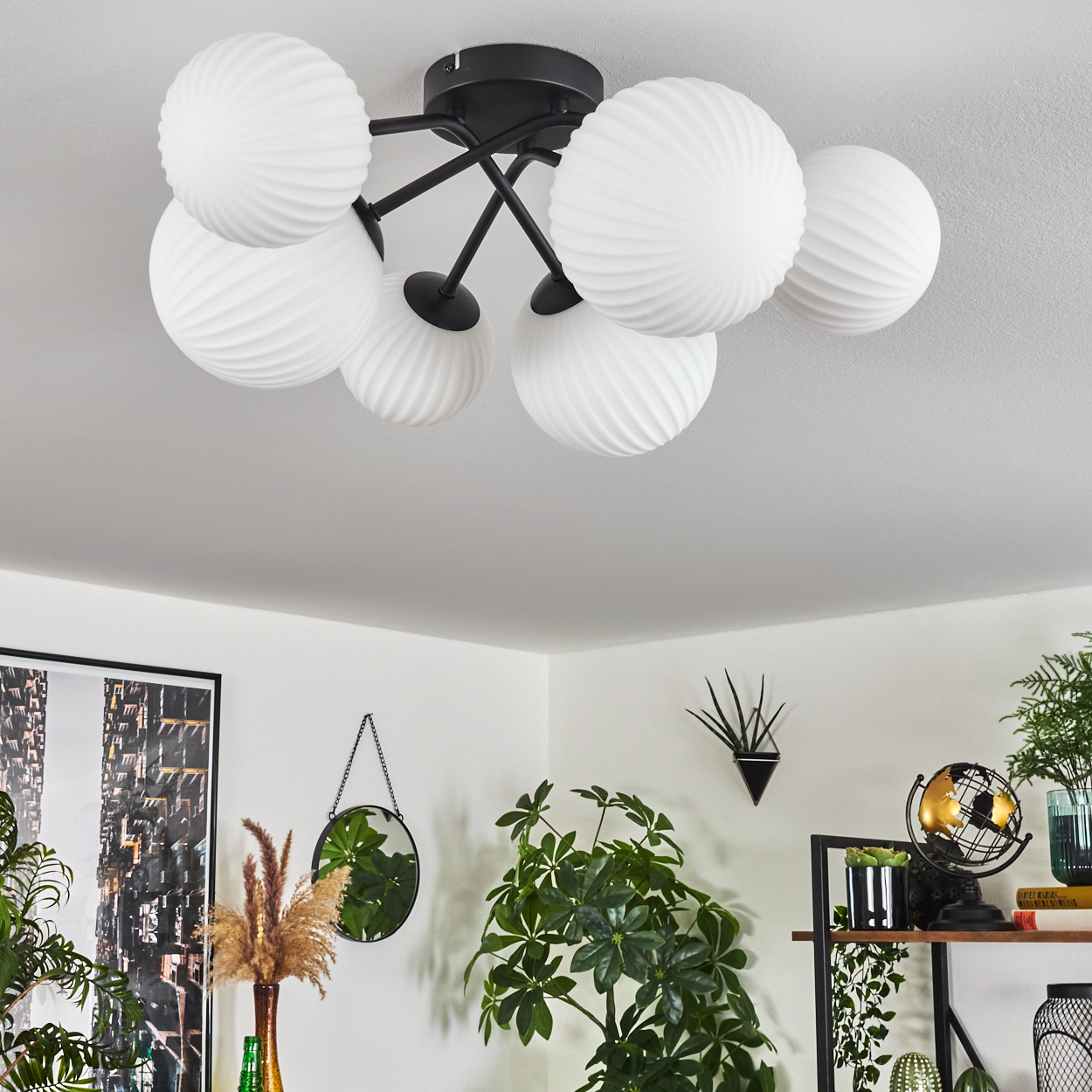 Eine Deckenleuchte mit weißen kugelförmigen Lampen. Der Raum hat Pflanzen, einen Spiegel, ein Gemälde und ein Regal mit Dekorationen.