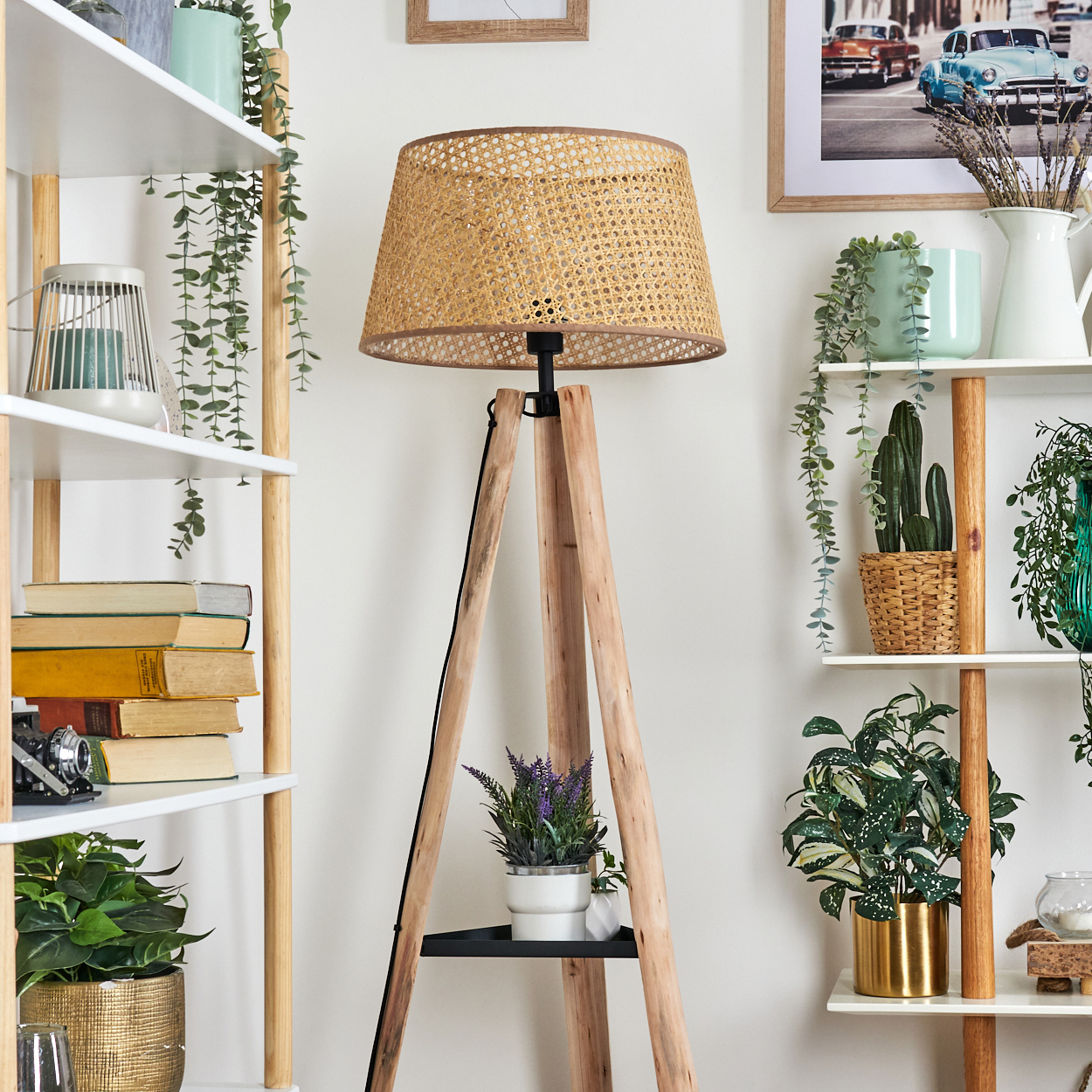 Eine Holzstativlampe mit gewebtem Schirm steht inmitten von Regalen mit Pflanzen, Büchern und Dekorationsartikeln vor einer weißen Wand.