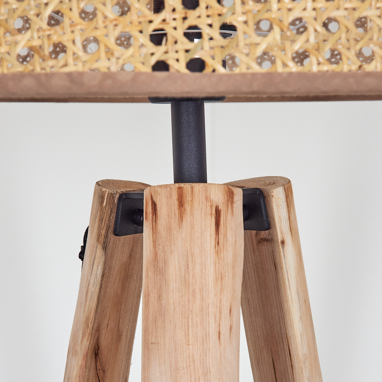 Nahaufnahme eines Holzlampenfußes. Er hat drei Beine und eine schwarze Metallstange. Der Lampenschirm ist aus geflochtenem Rattan.