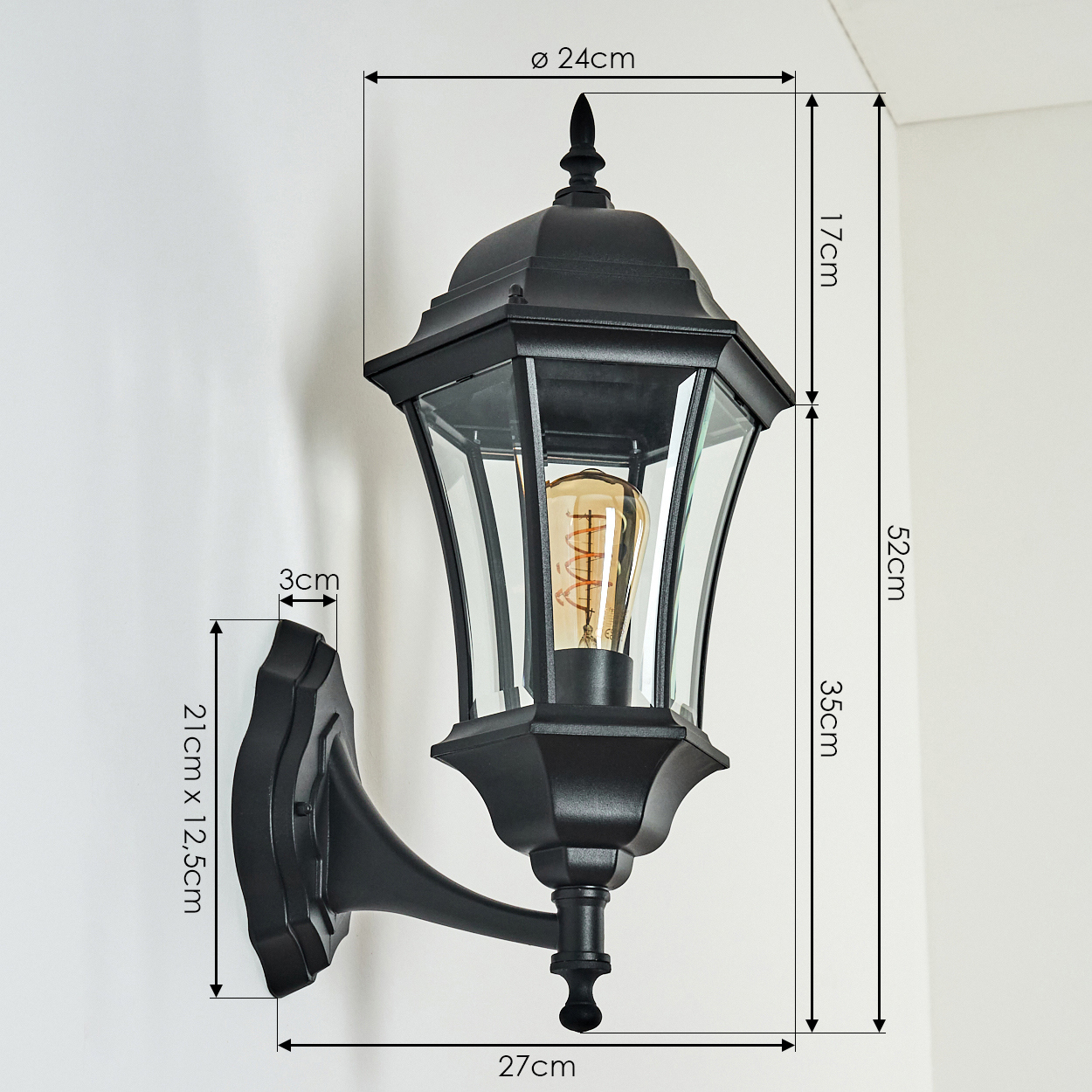 Schwarze Außenwandleuchte mit Glasscheiben und sichtbarer Glühbirne. Abmessungen werden ebenfalls angezeigt. An einer weißen Wand montiert.