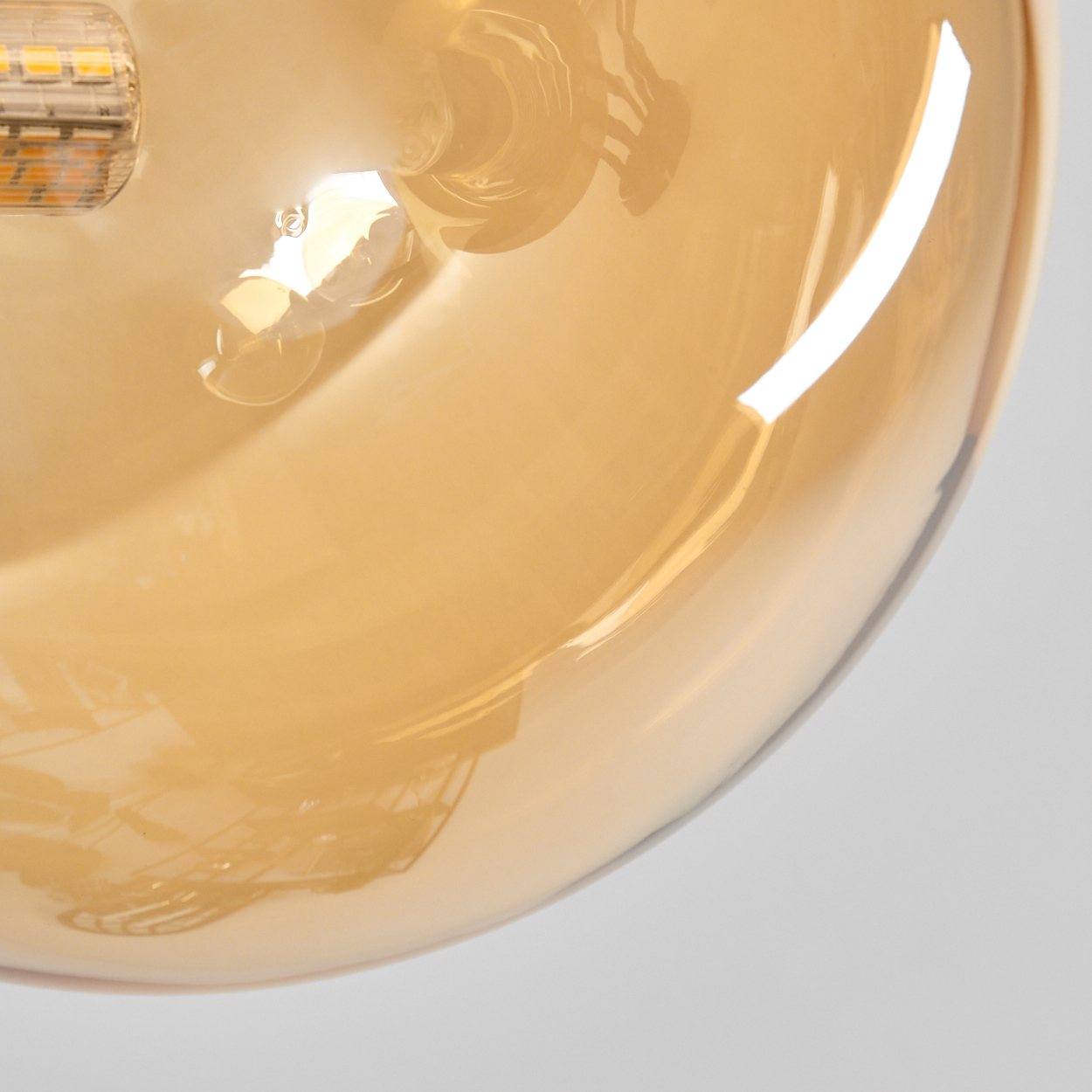 Nahaufnahme einer Glühbirne. Die Birne ist transparent bernsteinfarben und reflektiert Licht. LED-Elemente sind links sichtbar. Weißer Hintergrund.