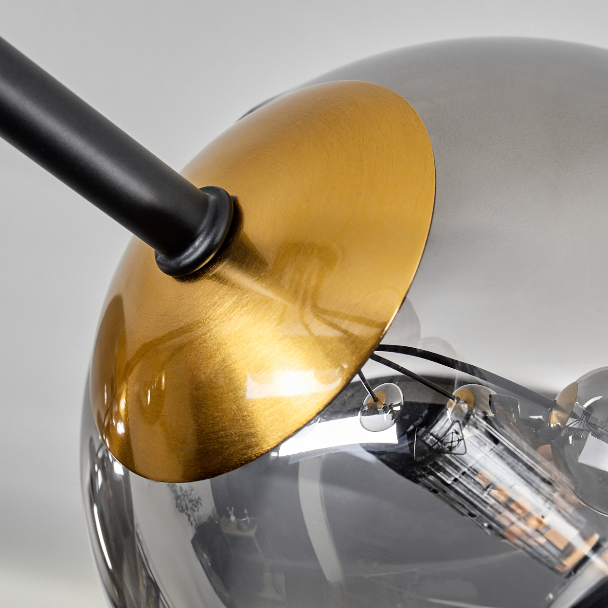 Nahaufnahme einer modernen Lampe. Sie hat einen goldfarbenen Metallschirm und eine rauchige Glaskugel mit schwarzem Arm und sichtbaren Glühbirnen.