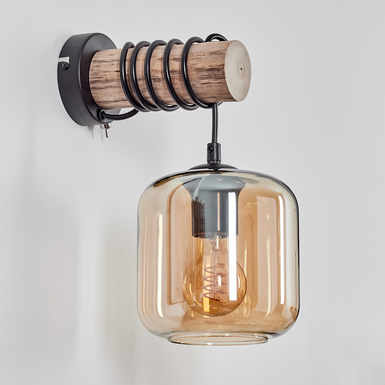 Eine Wandleuchte mit Holzbalken, schwarzer Metallspirale und Glasschirm mit sichtbarer Glühbirne.