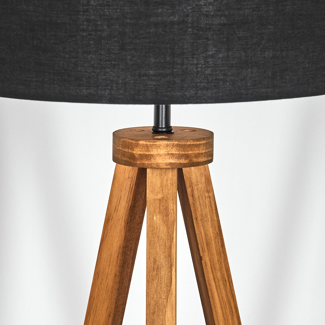 Eine Stehlampe mit Holzstativ und schwarzem Lampenschirm. Die Lampe hat einen runden Holzfuß und drei Holzbeine. Weißer Hintergrund.