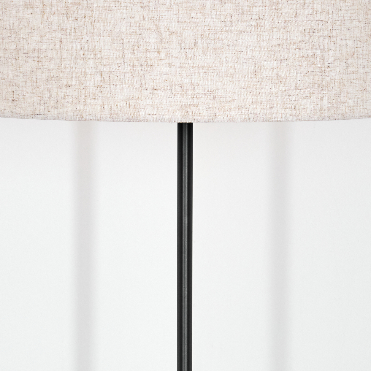 Nahaufnahme einer Lampe. Beiger Lampenschirm über einem schwarzen Pfosten vor weißer Wand. Schatten an der Wand.